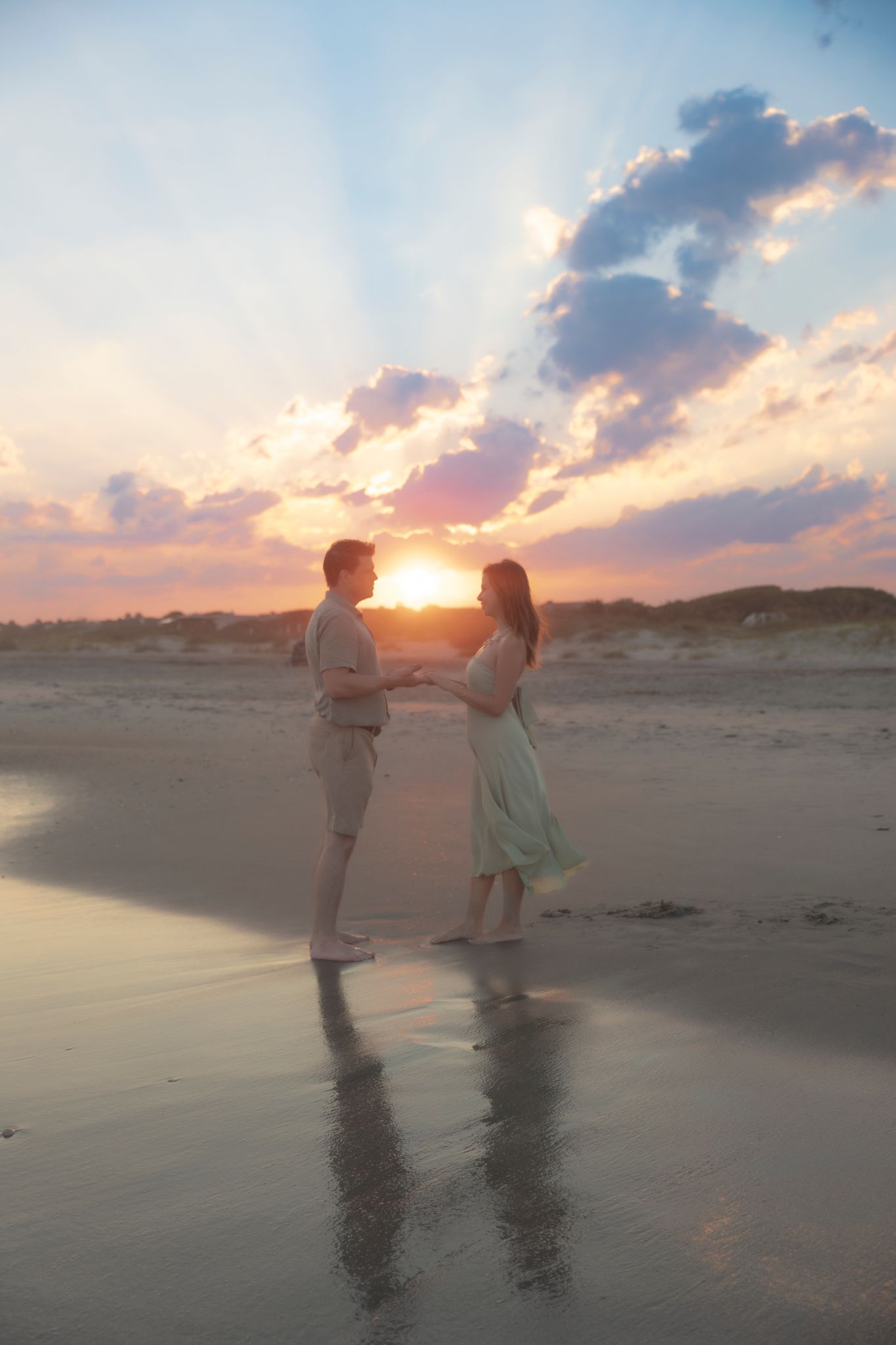 Couple holding hands on a reflective beach at sunset with dramatic golden rays bursting through clouds in Charleston, SC.