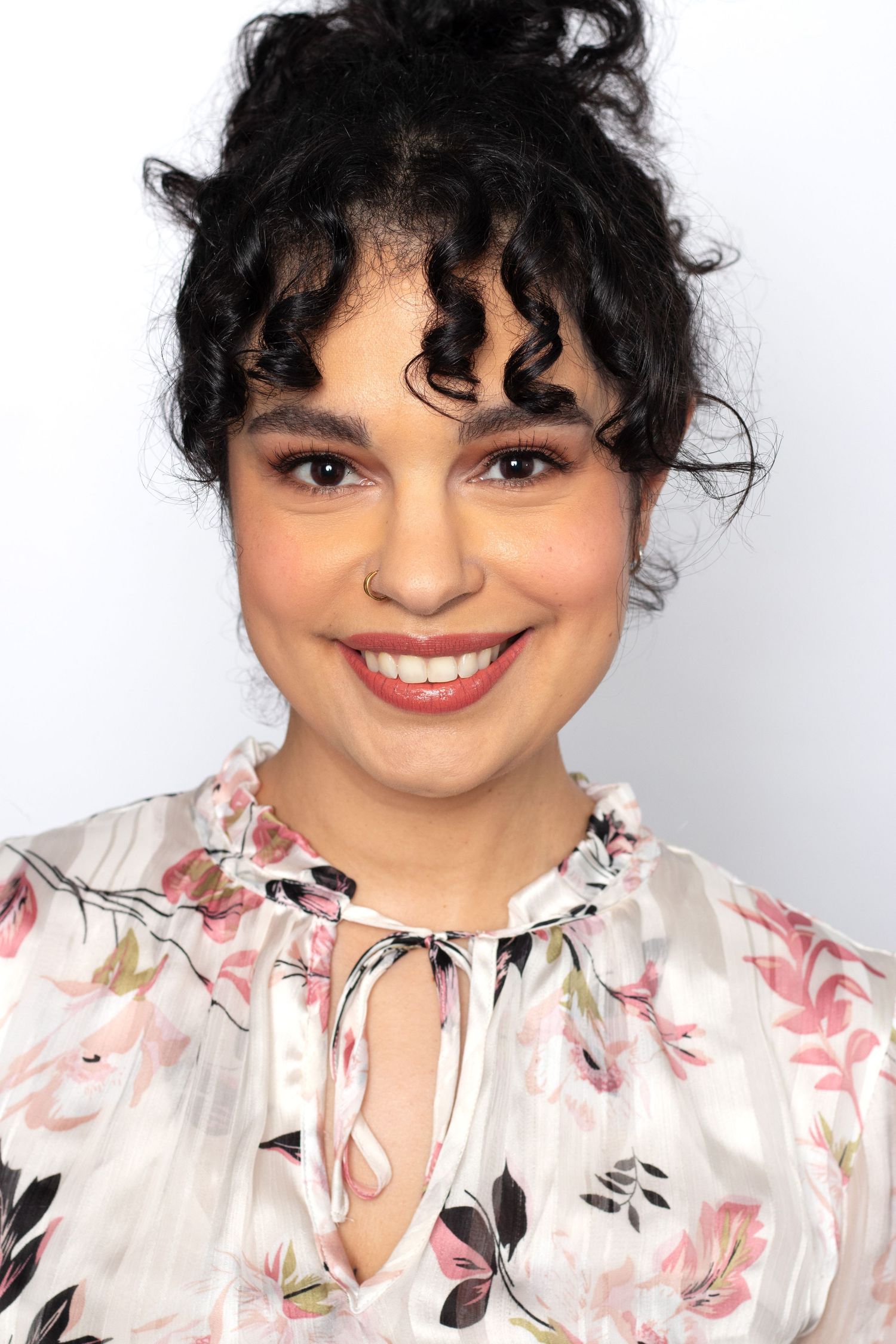 Smiling young woman with curly black hair wearing a floral blouse poses for a professional actor headshot.