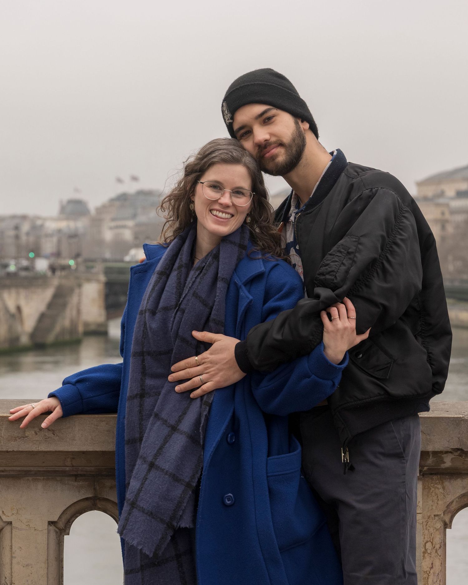Smiling couple embracing on bridge overlooking misty Paris river.