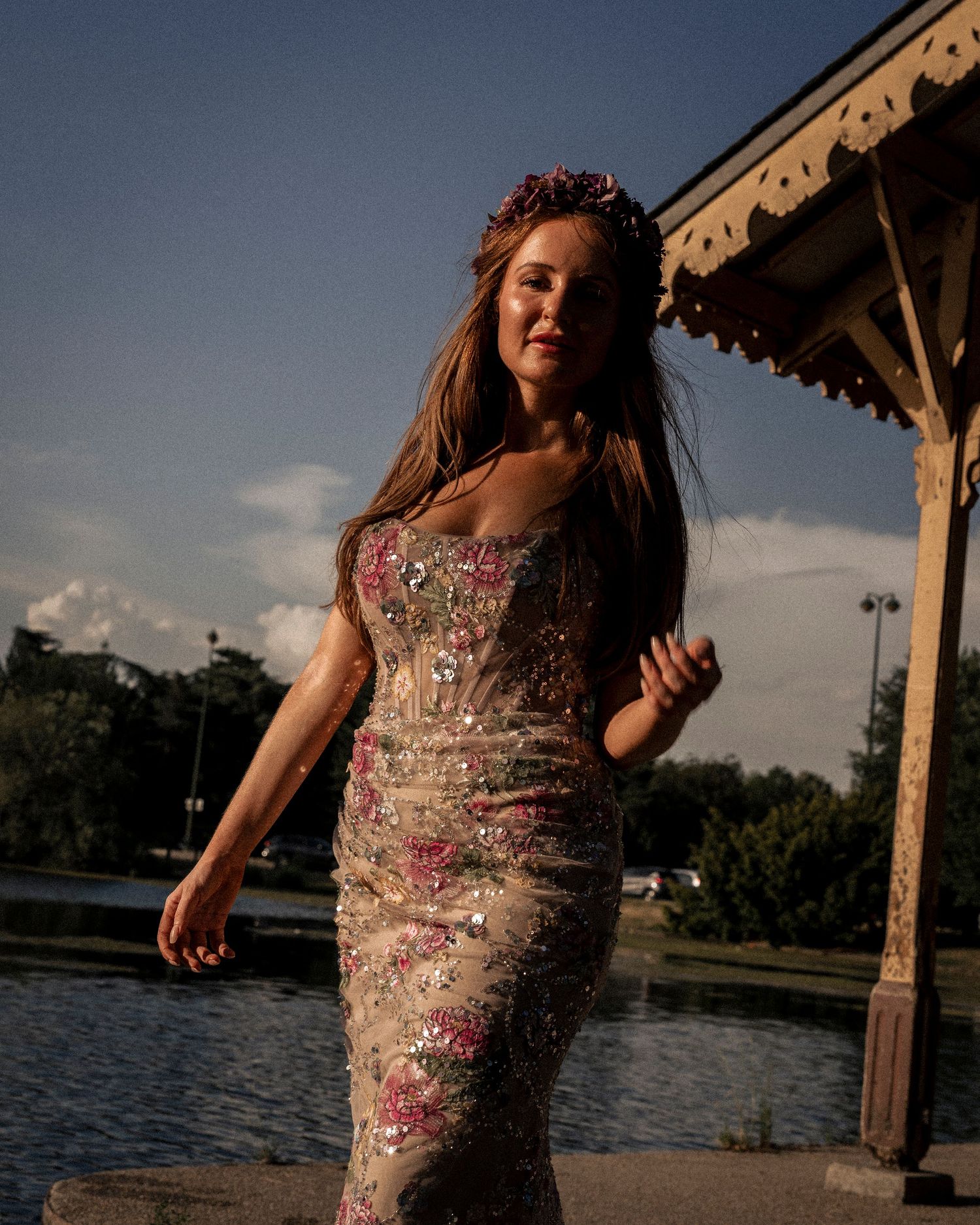 Woman in a floral embroidered strapless gown with a flower crown posing by a gazebo.
