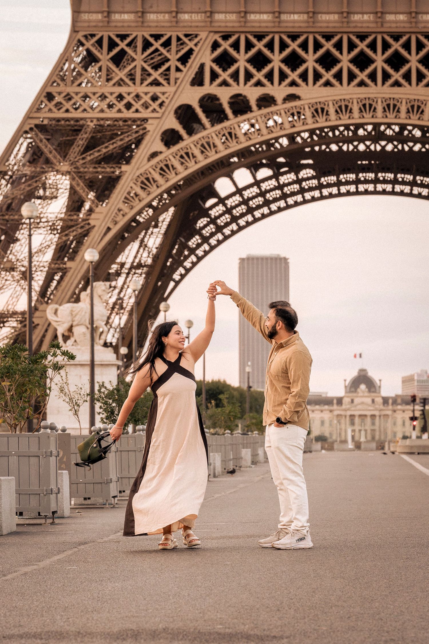 Couple dancing together beneath the Eiffel Tower in Paris, woman in elegant white dress spinning gracefully.