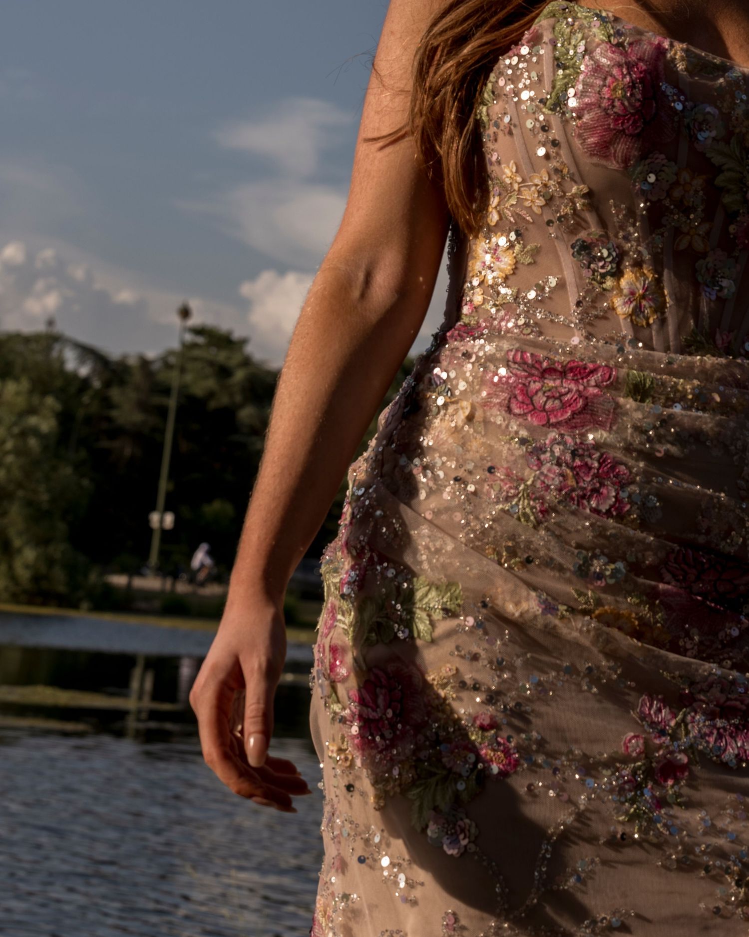 Close-up detail of a floral embroidered sequin gown worn outdoors near a lake.