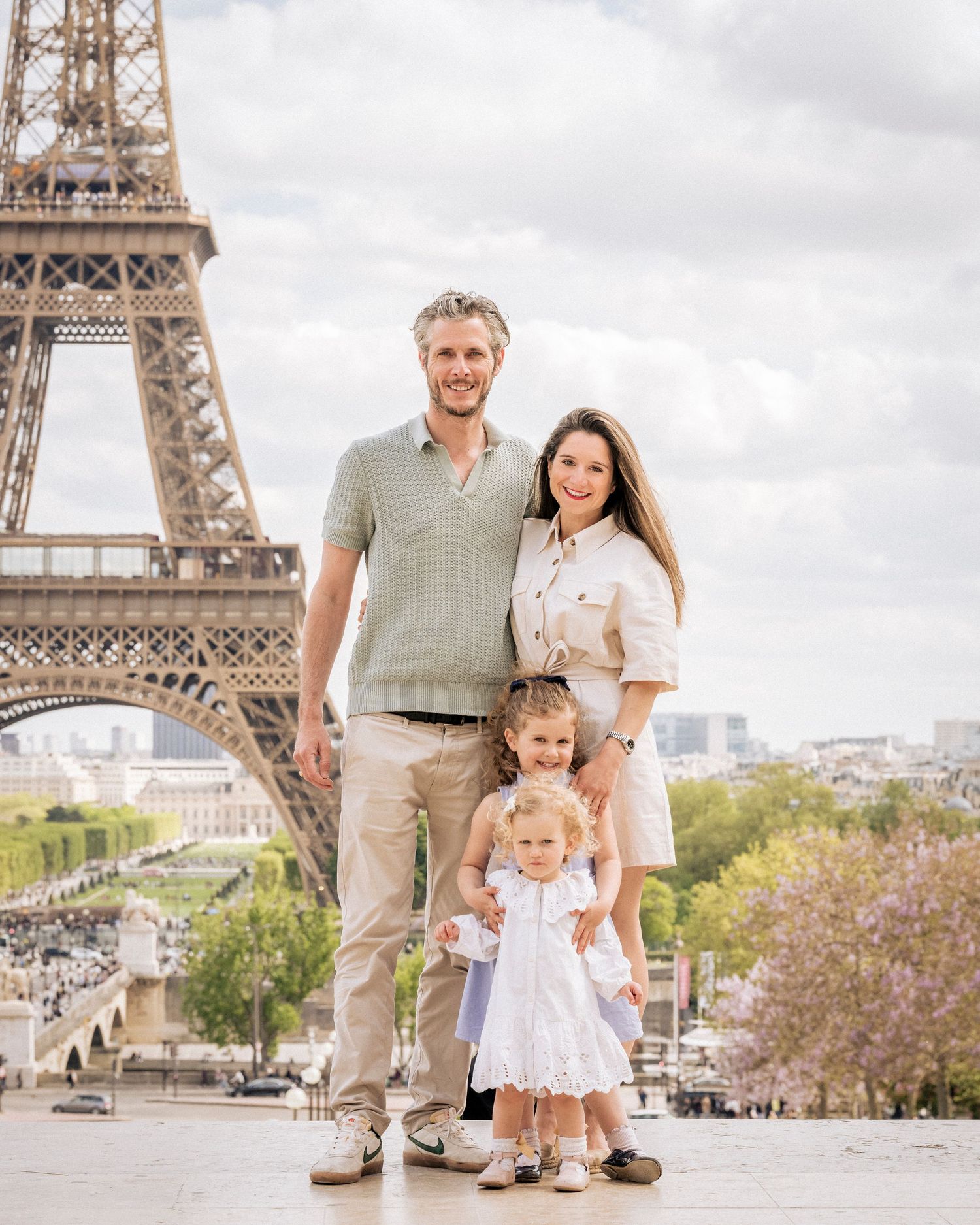 Family of three posing in front of the Eiffel Tower in Paris on a cloudy spring day.