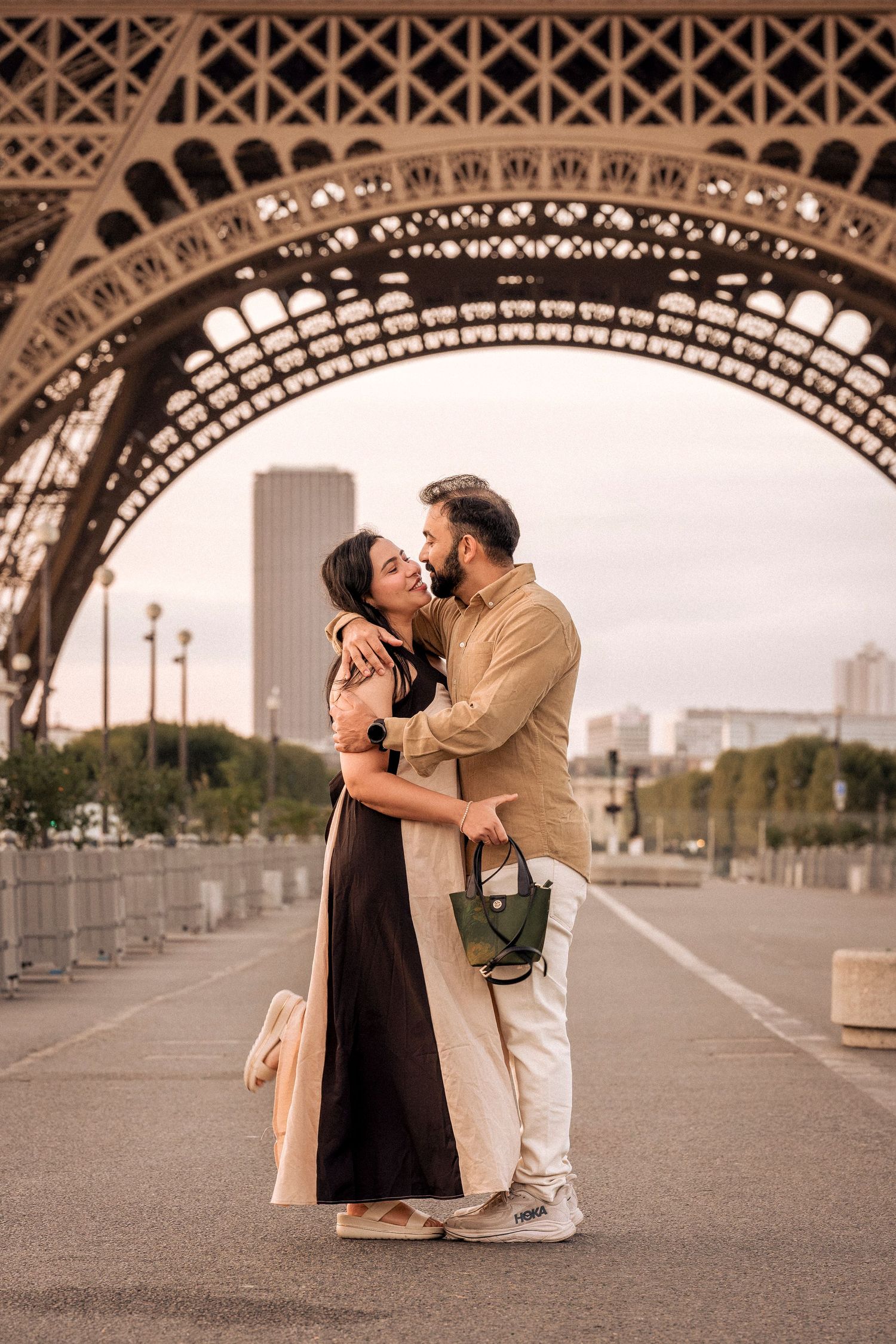 Romantic couple embracing and kissing beneath the iconic iron arches of the Eiffel Tower Paris.