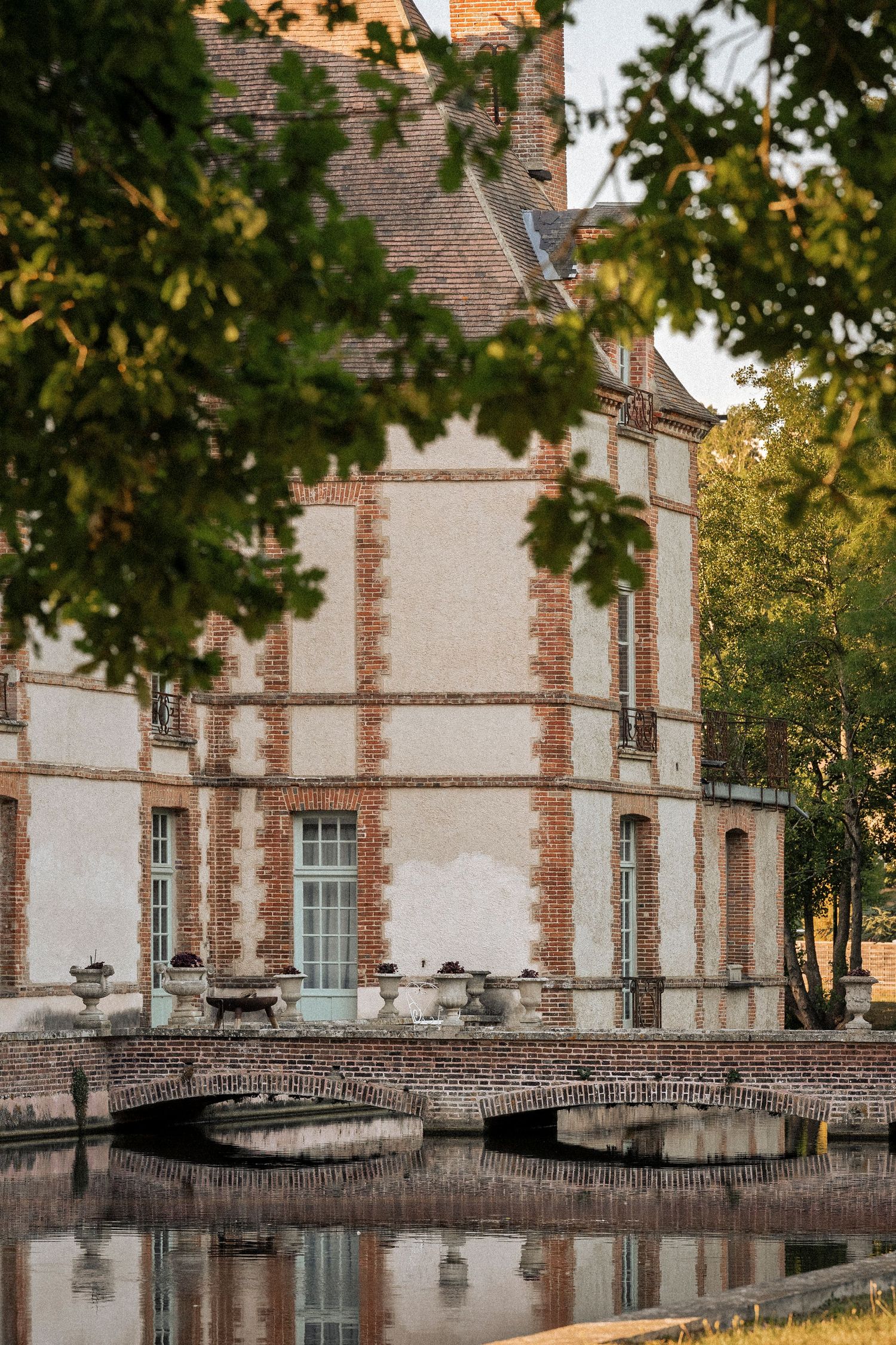 Elegant French chateau with brick and stone facade, arched bridge reflected in surrounding moat.