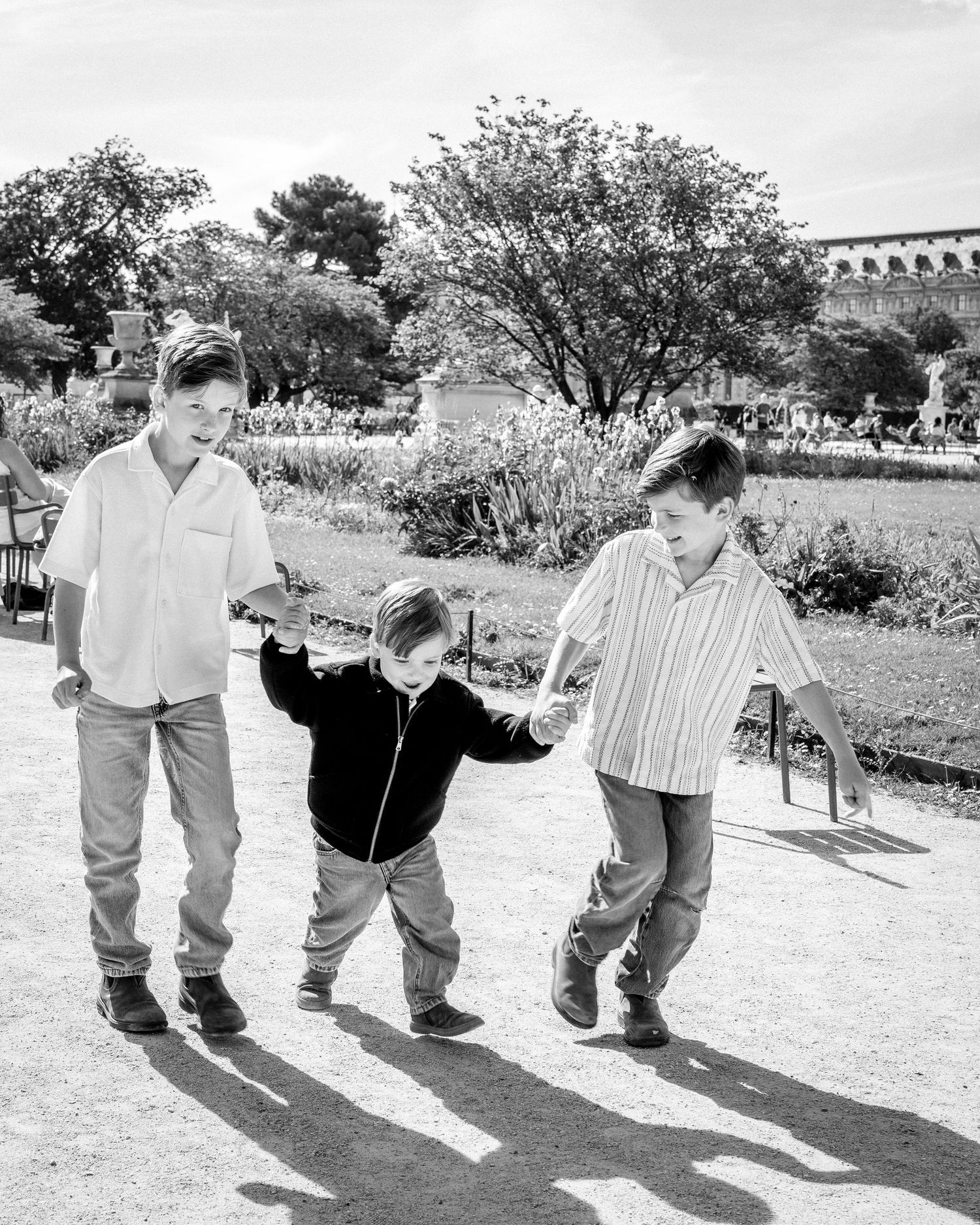 Three boys walking hand in hand in sunny park, black and white photo.