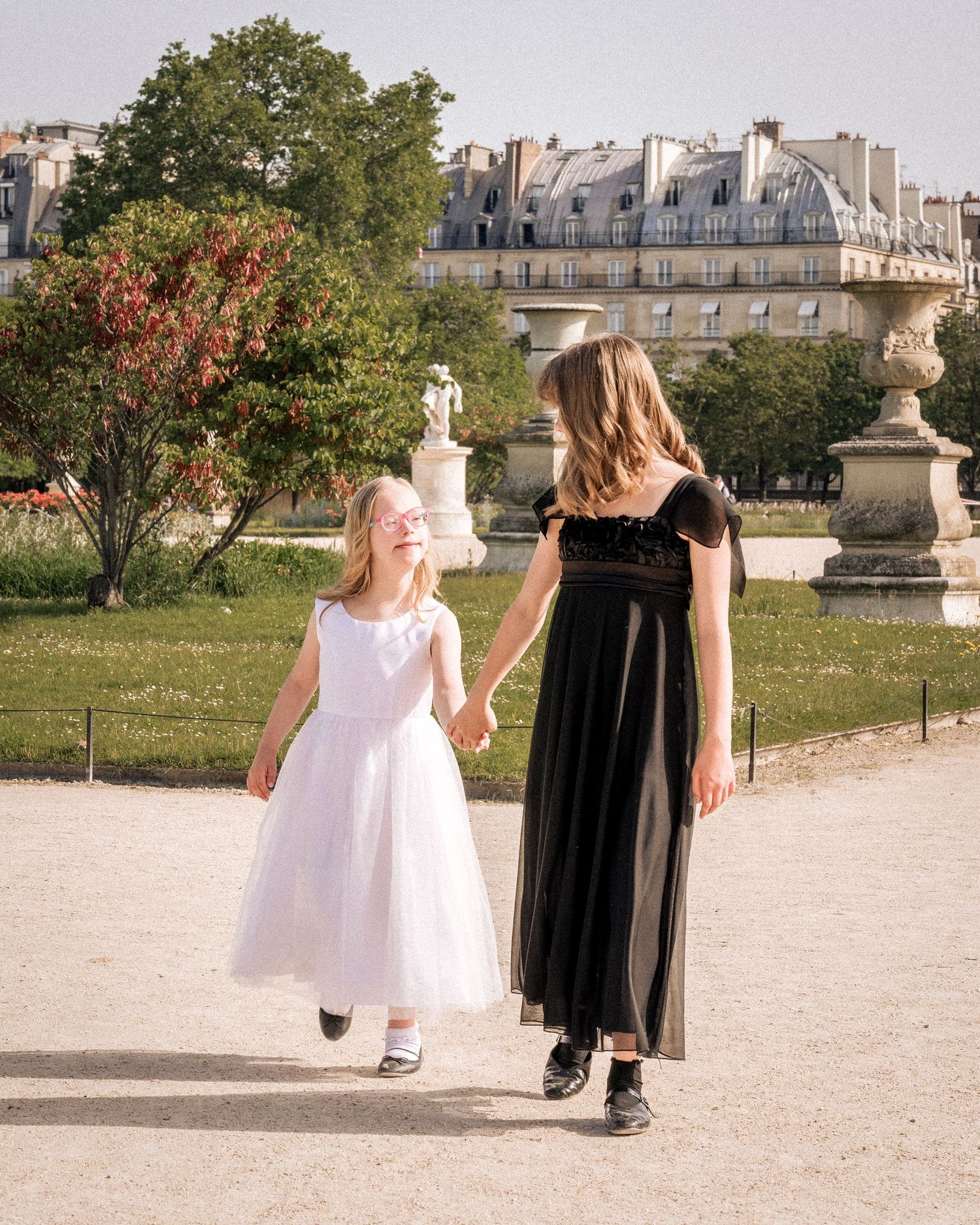 Two girls in white and black dresses holding hands walking in Tuileries Garden, Paris.