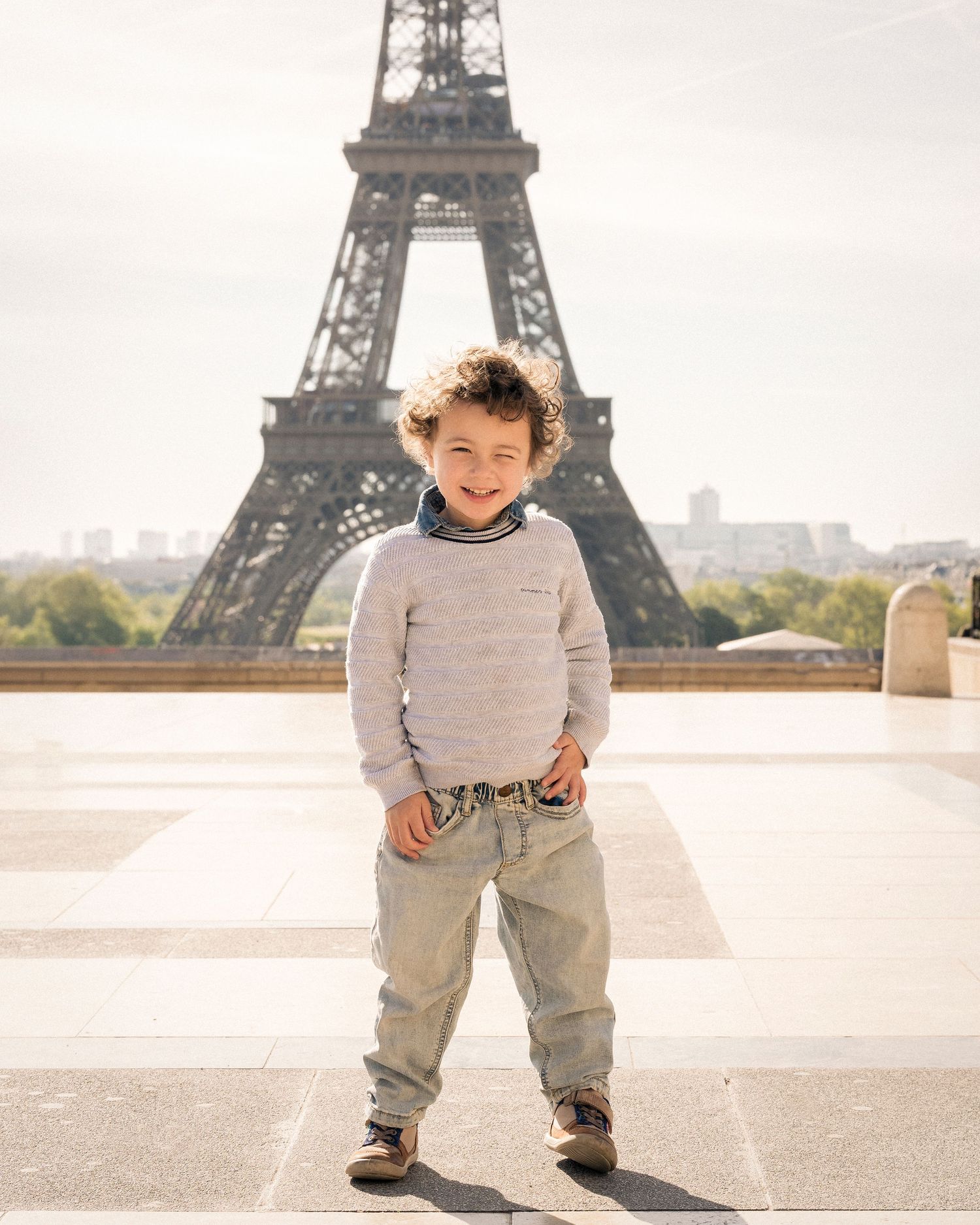 Happy young boy smiling in front of the Eiffel Tower on a bright sunny day in Paris.