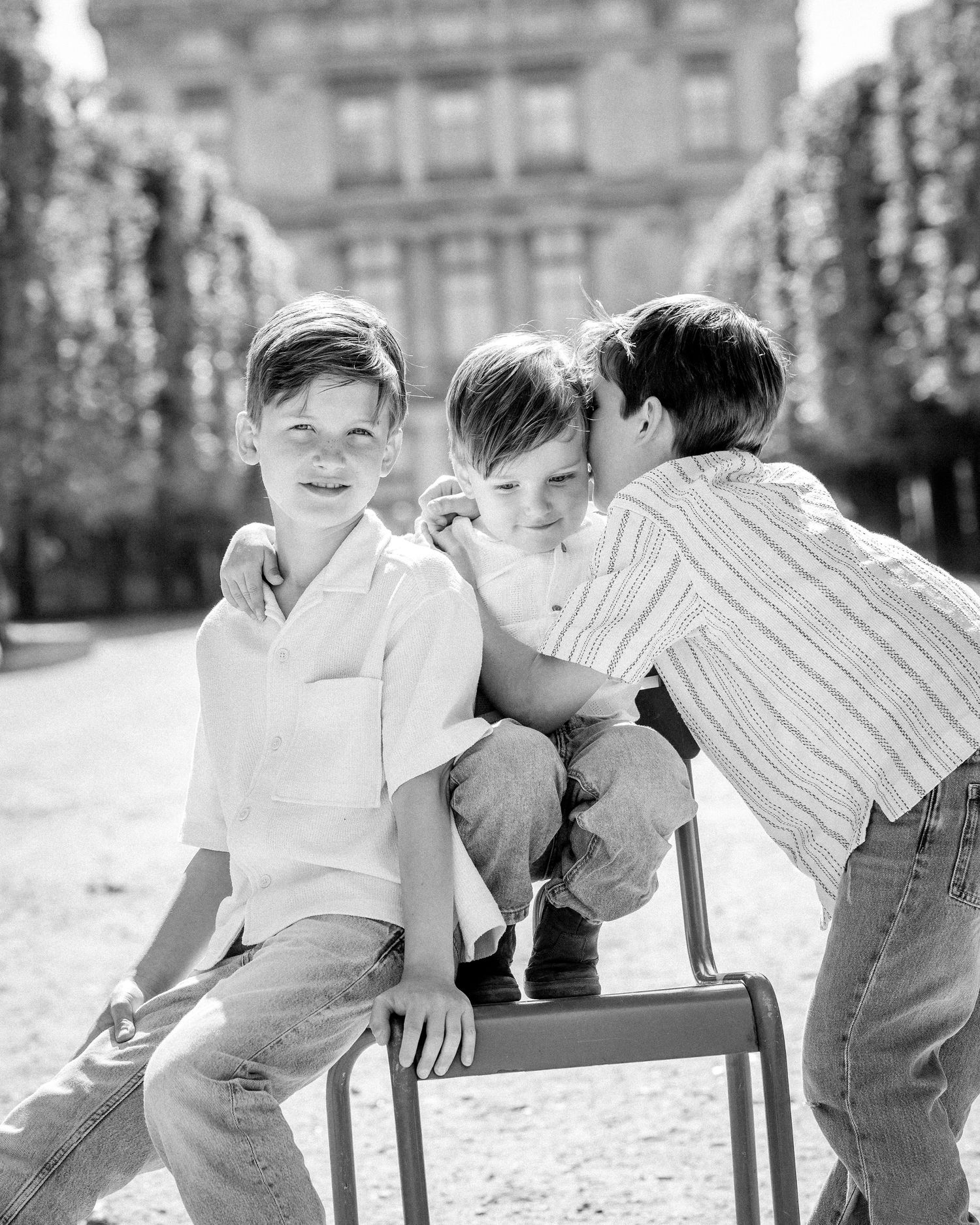 Black and white photo of three brothers sharing a sweet moment on a chair in a Paris garden.