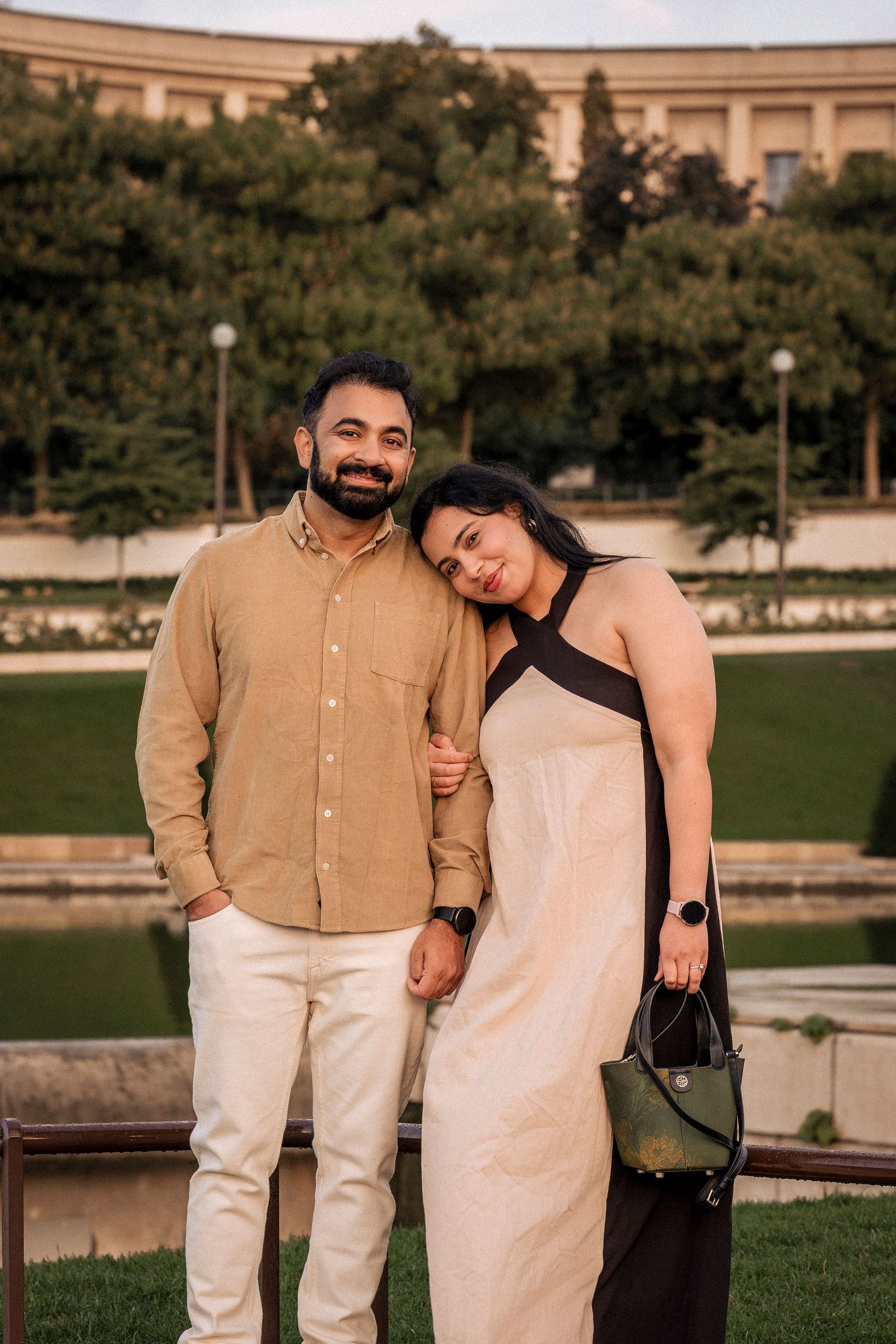 Smiling couple posing in a sunny park, man in beige shirt and woman in elegant dress.