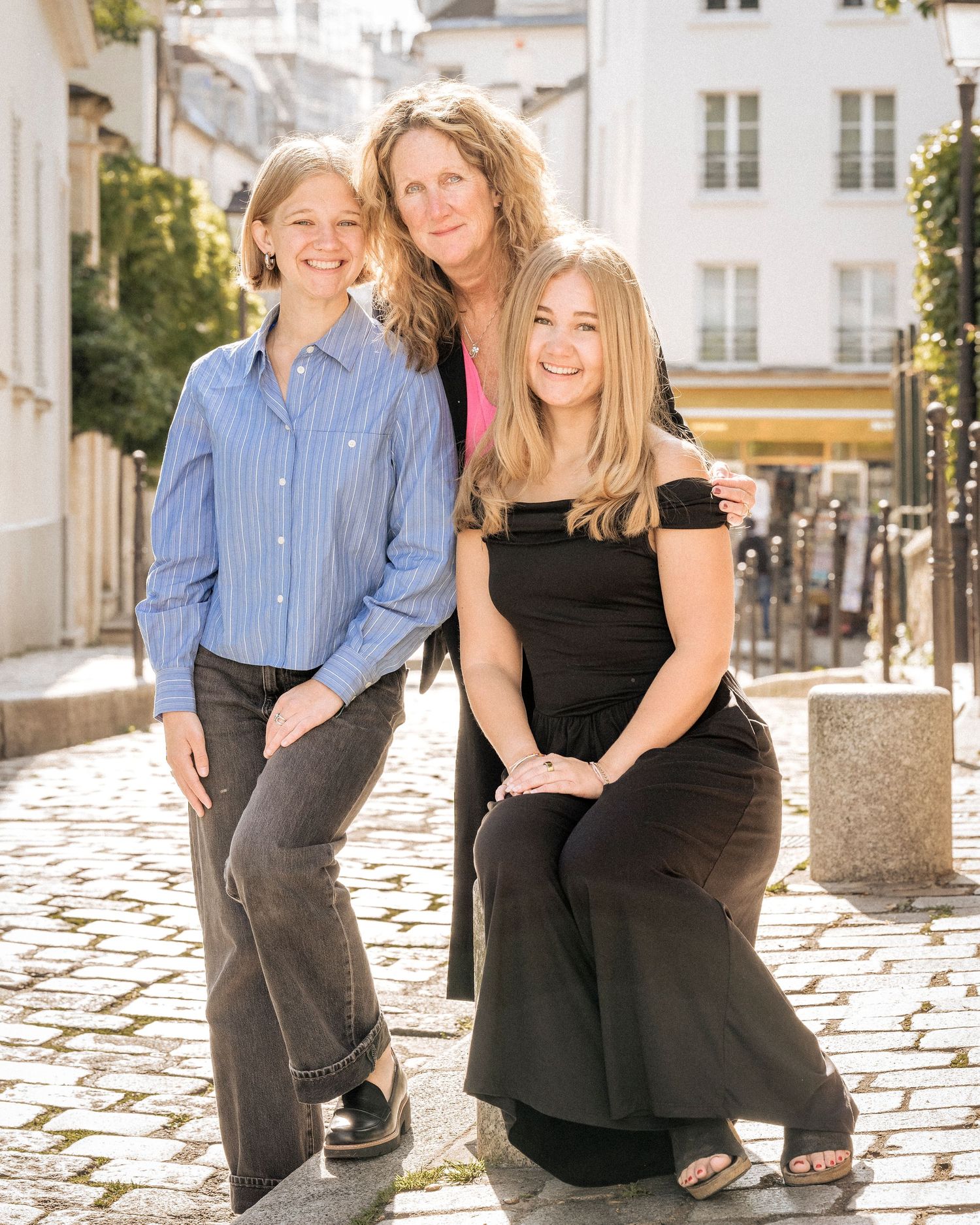 Three generations of women posing together on charming cobblestone street in Paris.
