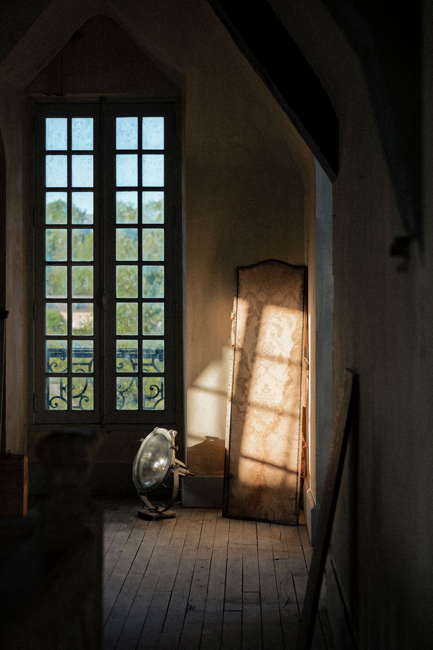 Sunlight streaming through tall French windows onto wooden floors in a rustic chateau room.