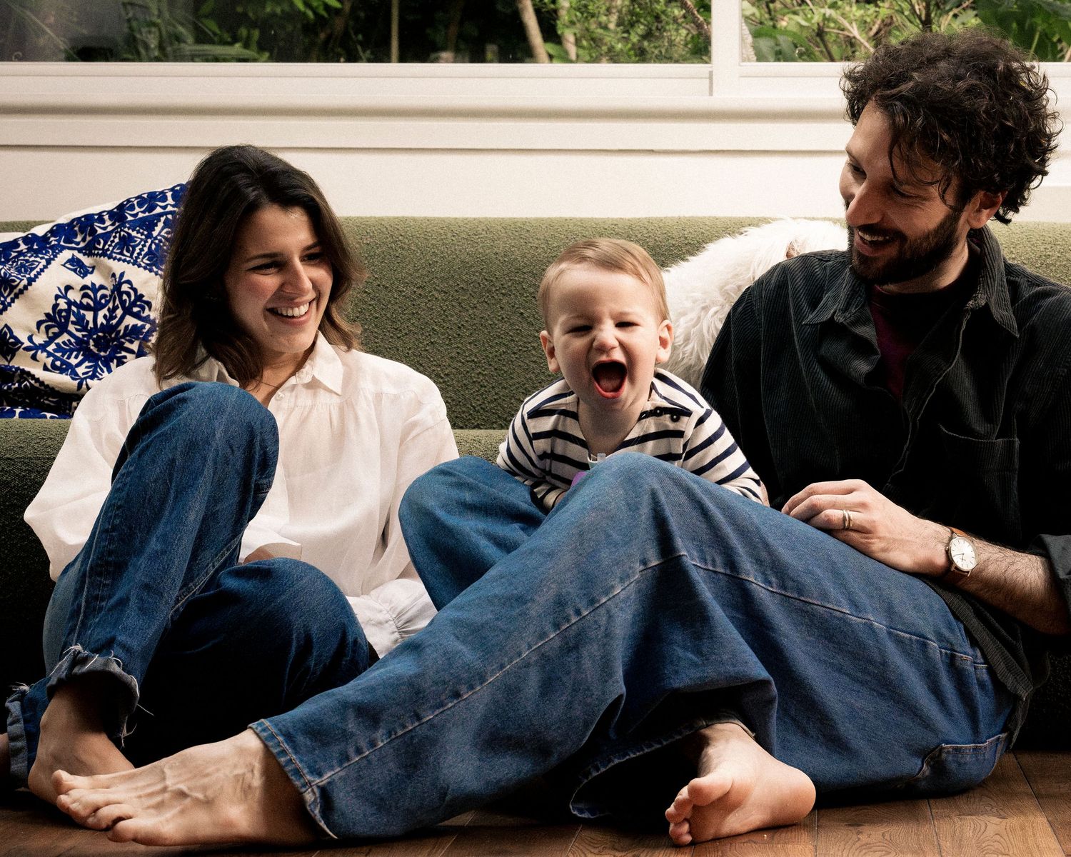 Happy family with baby sitting on floor laughing together in bright living room.