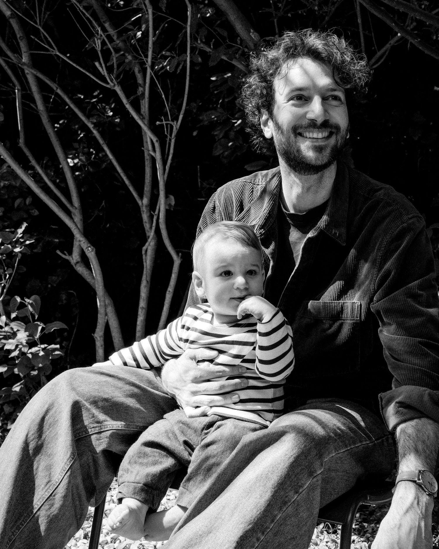Smiling father holding baby on lap outdoors, black and white portrait.