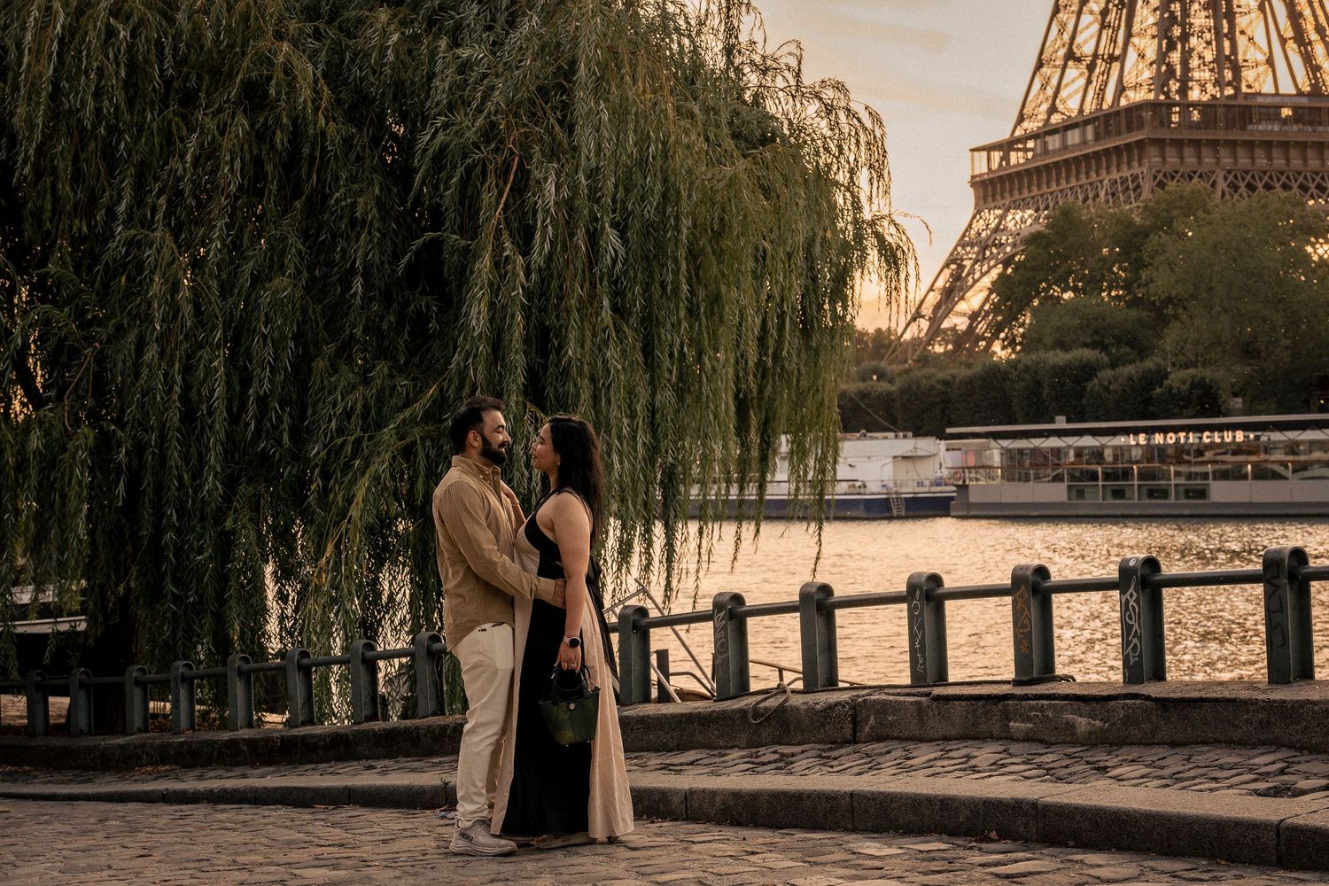 Romantic couple sharing a tender moment near the Eiffel Tower at golden sunset by the Seine River.