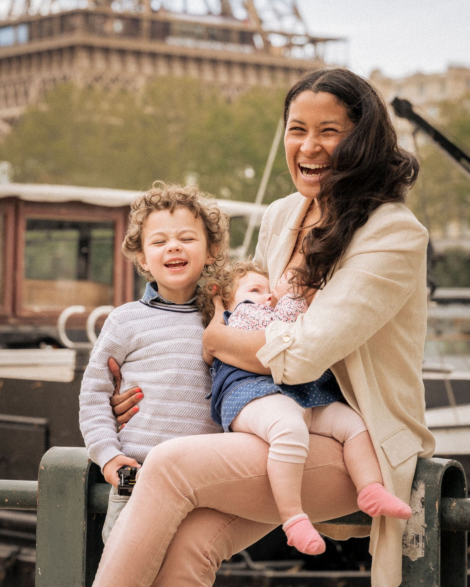 Laughing mother with two young children sitting near the Eiffel Tower in Paris.