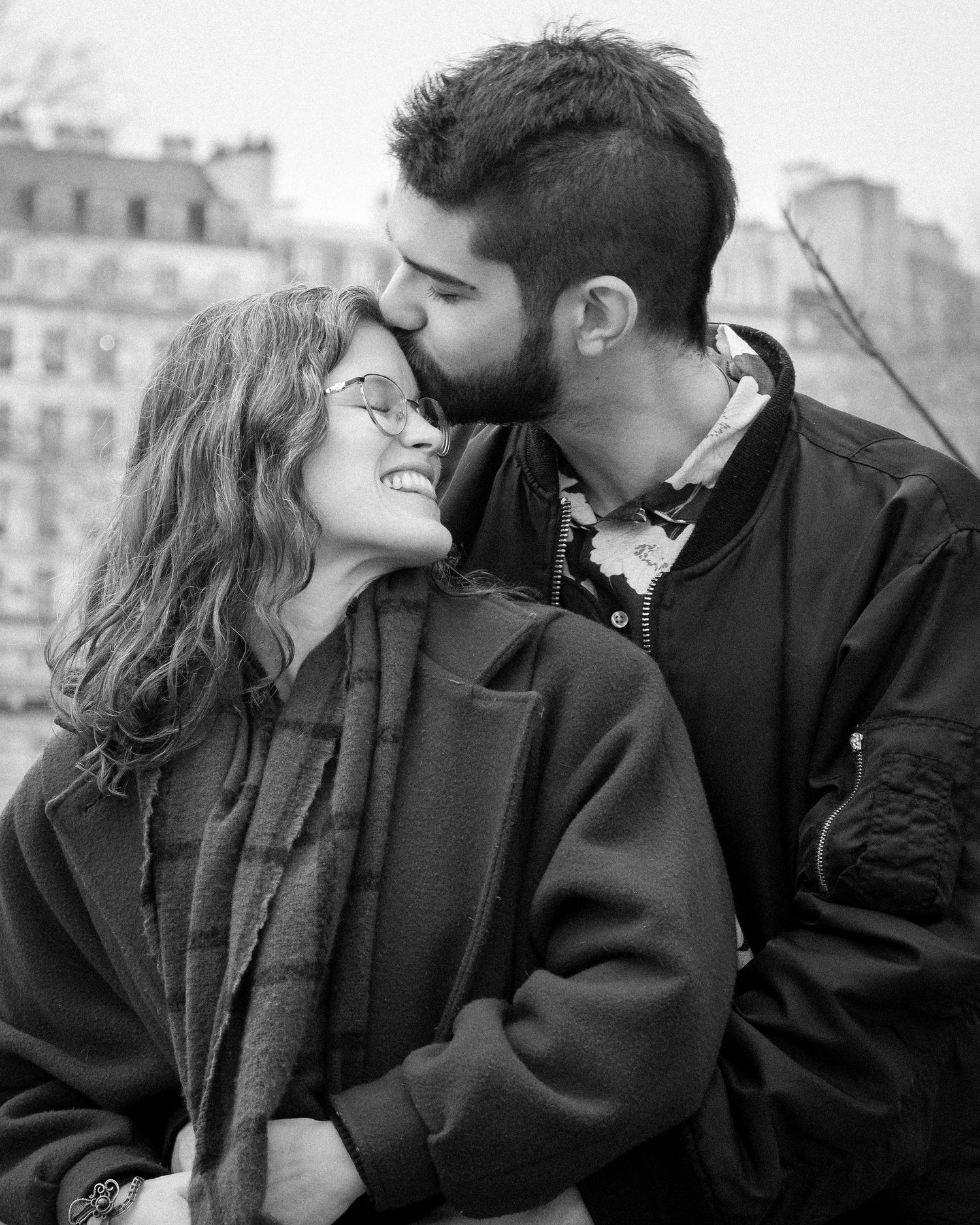 Black and white photo of a smiling couple sharing a tender kiss outdoors in Paris.
