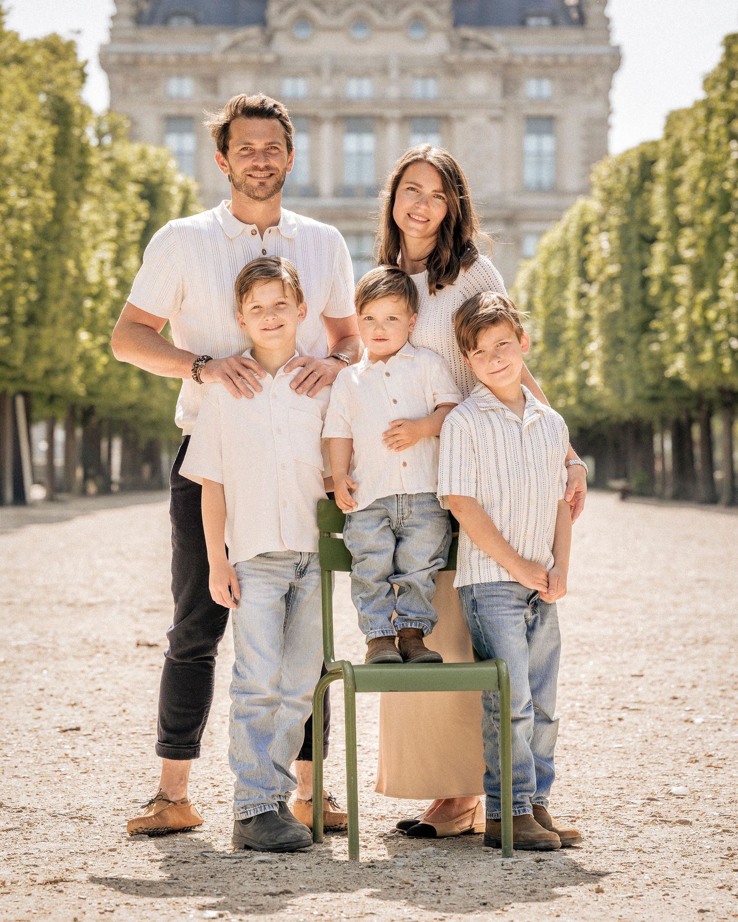 Happy family of five posing in sunny Tuileries Garden Paris with green chair.