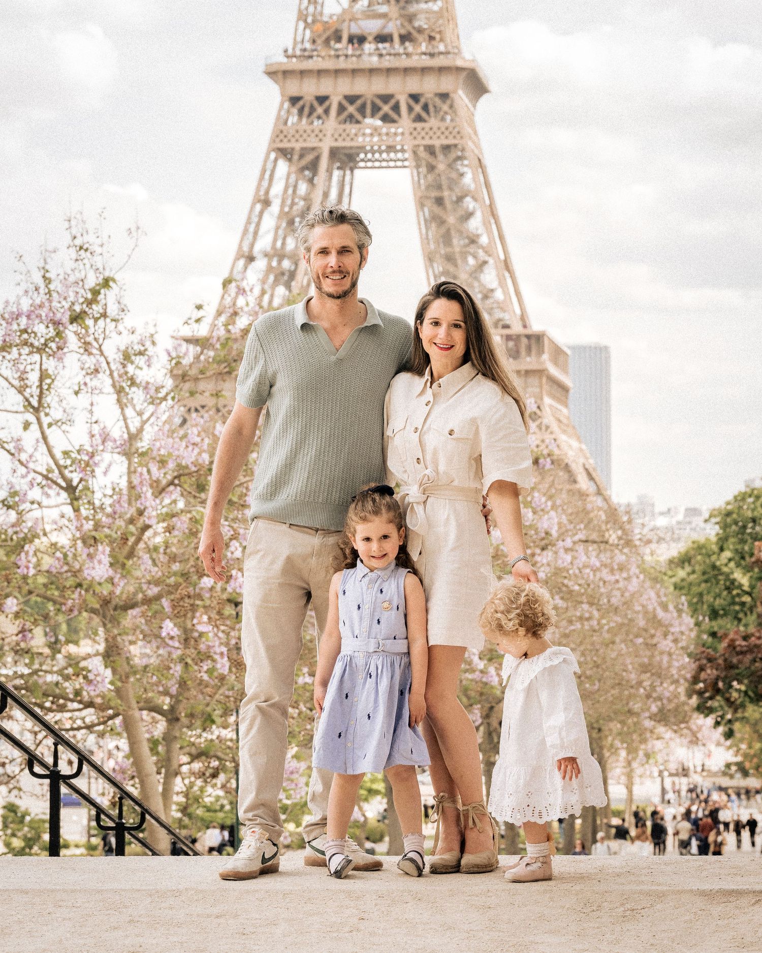 A family of four poses in front of the Eiffel Tower surrounded by blooming pink trees in Paris.