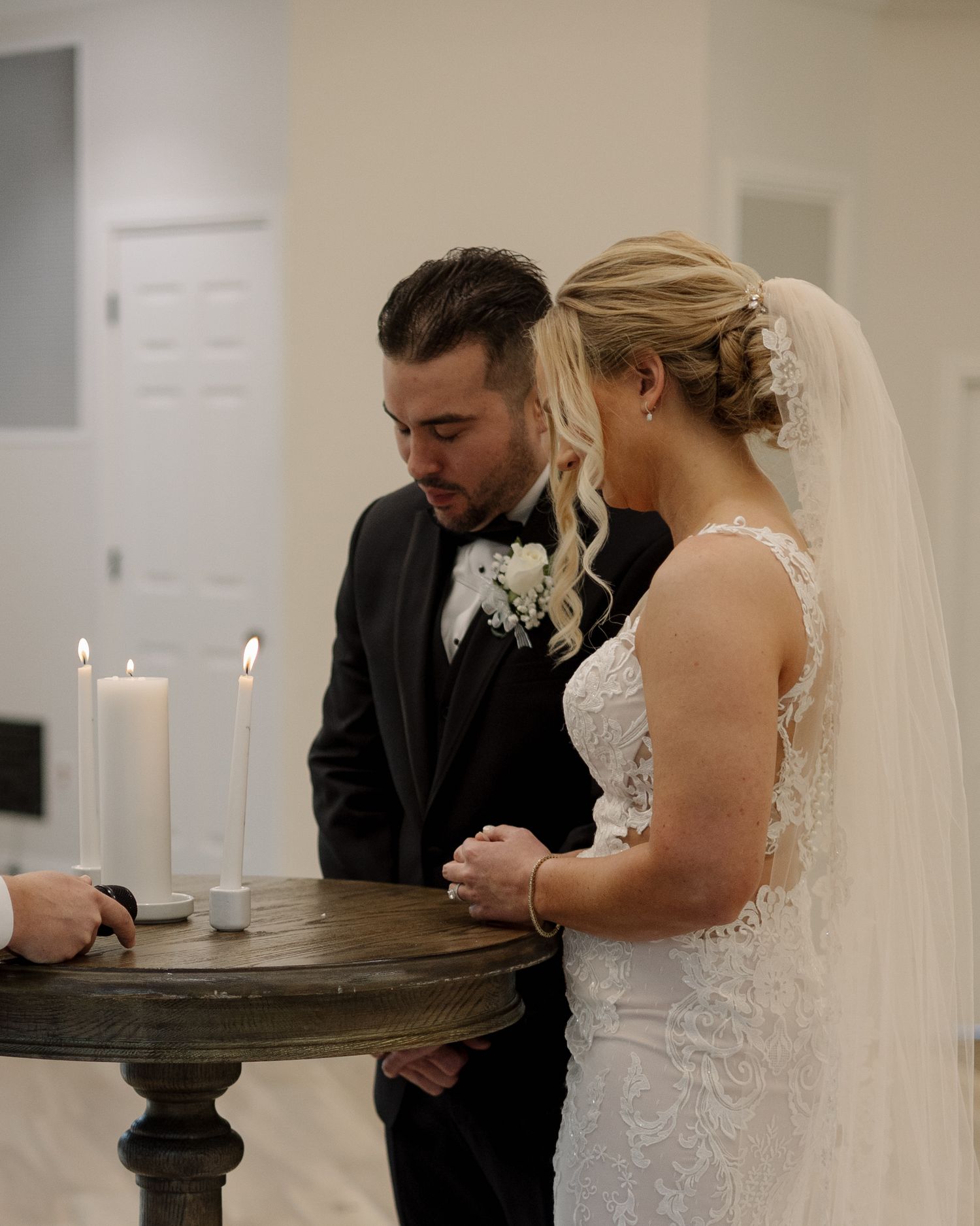 Bride and groom lighting unity candles during indoor wedding ceremony at elegant white venue.