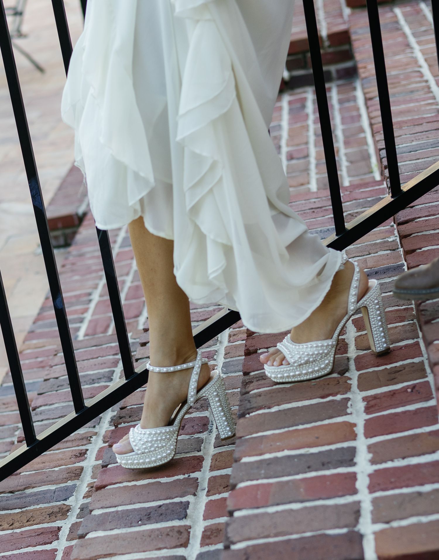Bride wearing pearl-embellished platform heels with layered white dress on brick outdoor staircase.