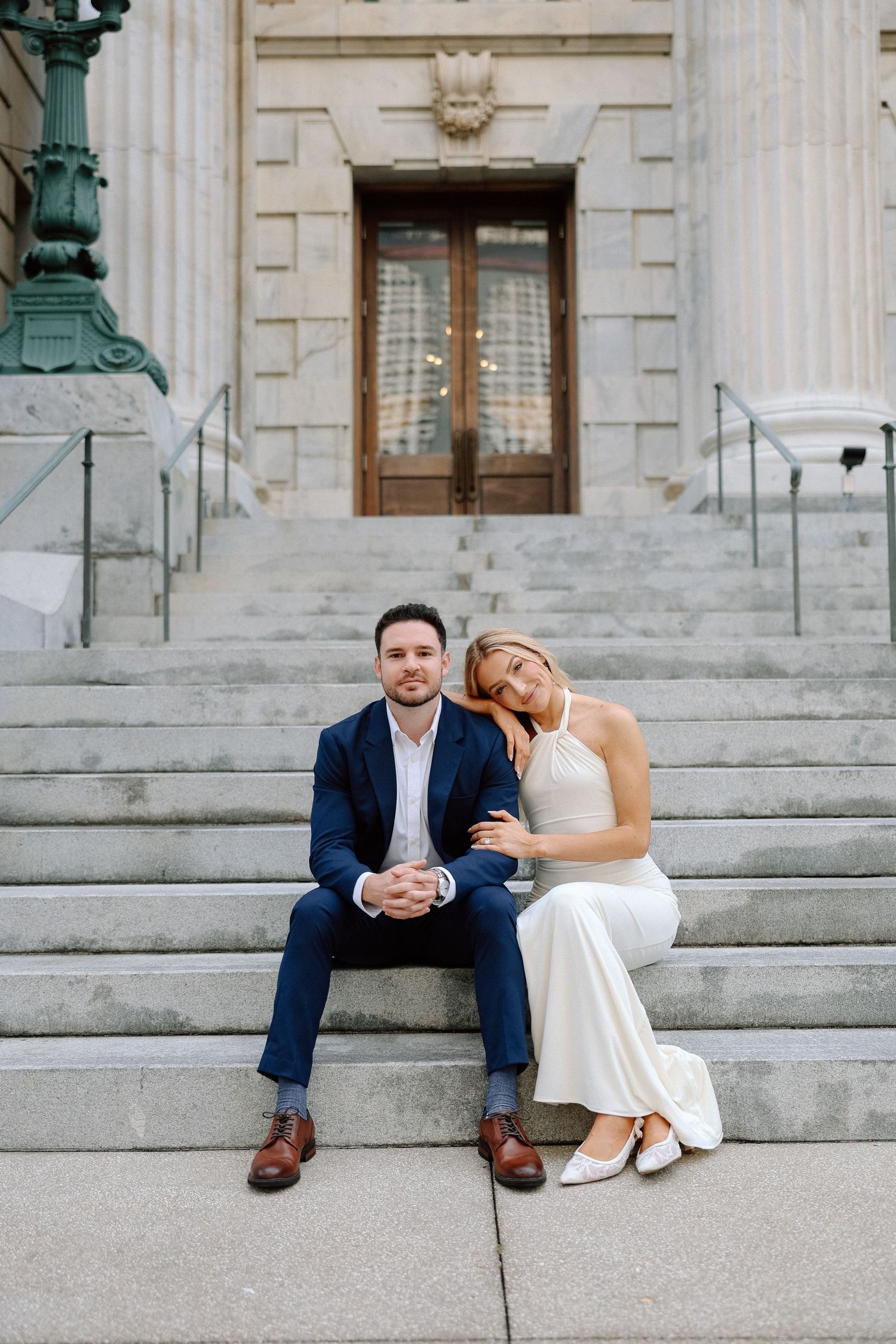 Bride and groom sitting together on steps of a neoclassical building during engagement session.