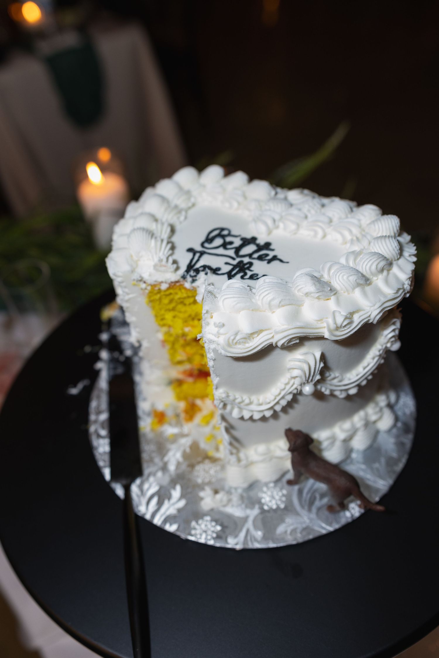 Heart-shaped white wedding cake with Better Together inscription sliced open revealing yellow layers inside.