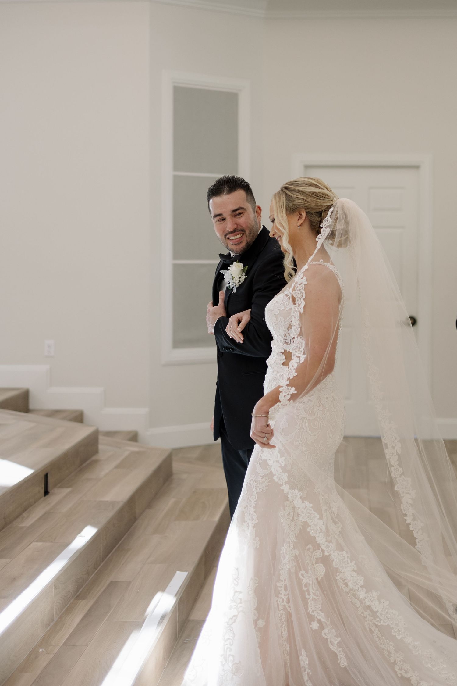 A groom smiles joyfully at his bride in a lace mermaid gown during their first look.