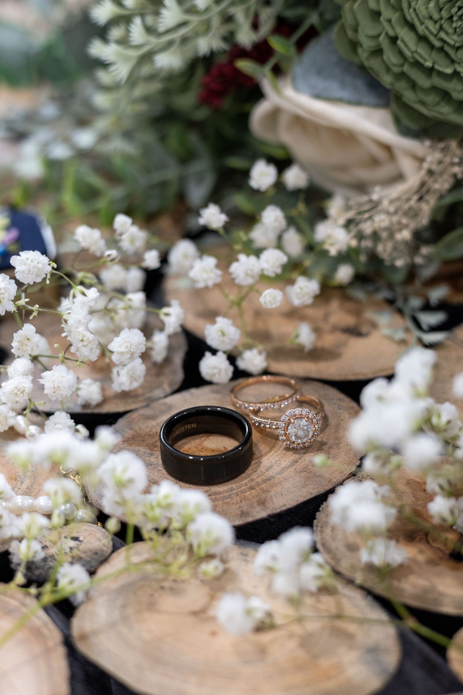 Wedding rings displayed on rustic wood slices surrounded by delicate white baby's breath flowers.