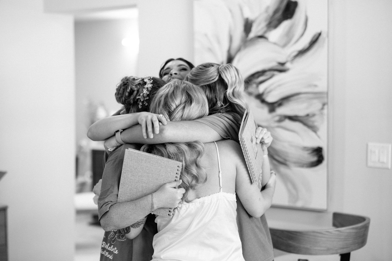 Black and white photo of bride sharing emotional group hug with bridesmaids during wedding getting-ready moment.
