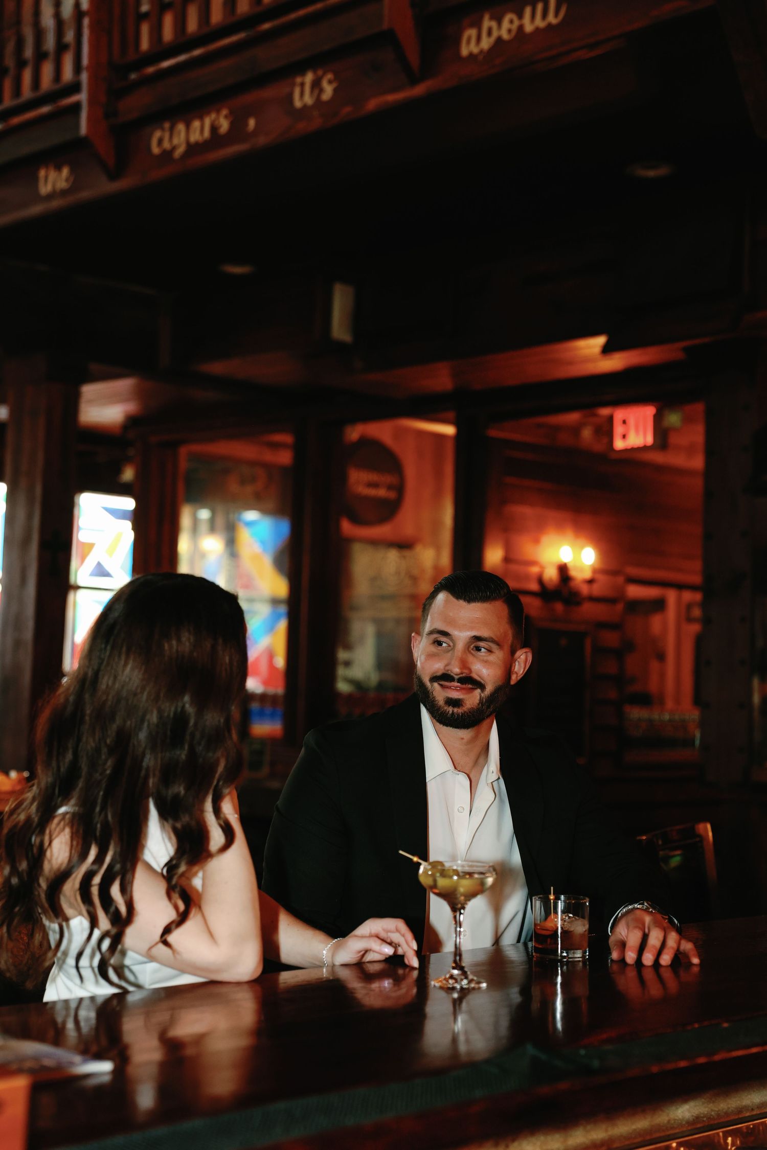 Couple sharing a romantic moment at a dimly lit bar with cocktails.