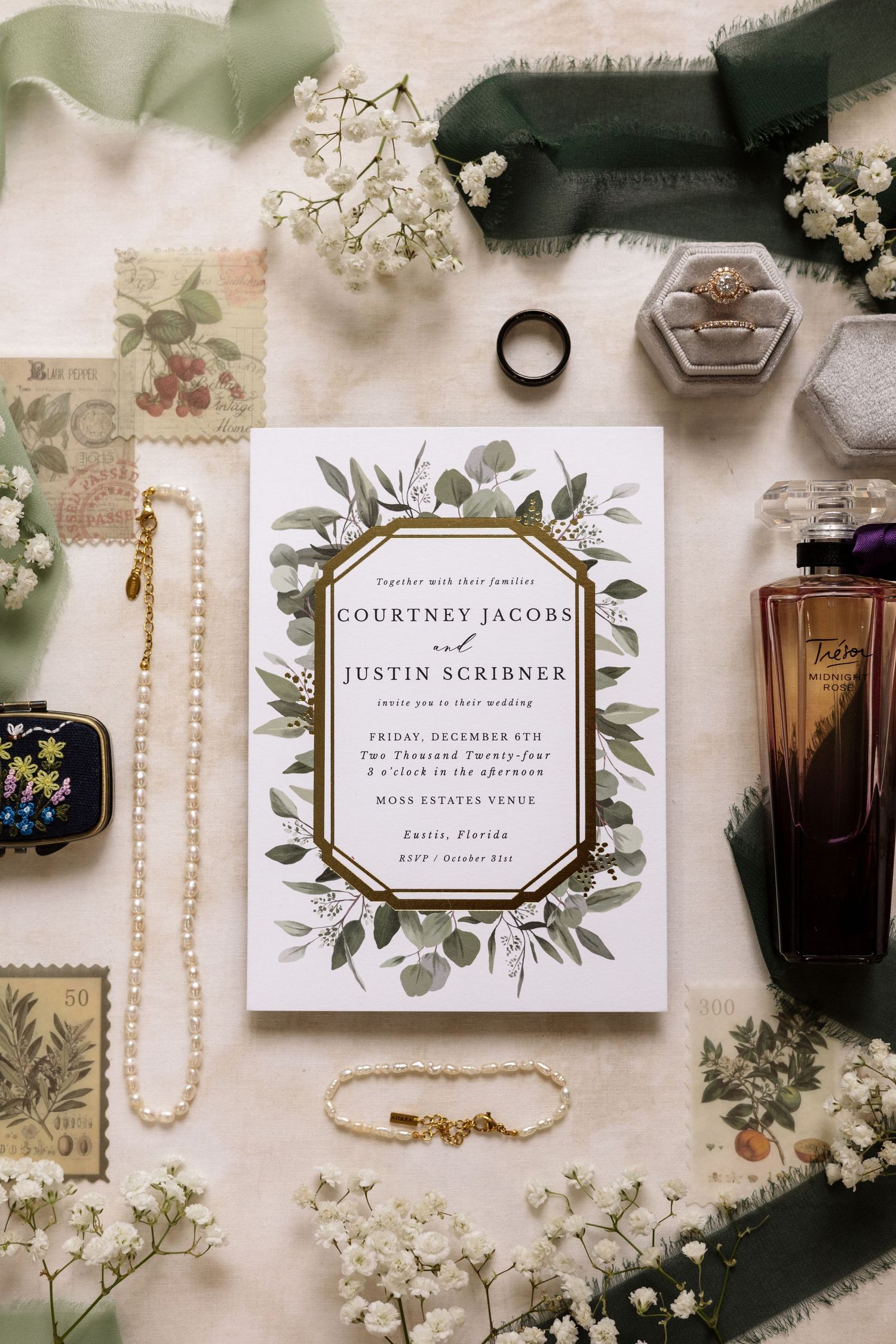 Elegant wedding invitation for Courtney Jacobs and Justin Scribner surrounded by jewelry and florals.