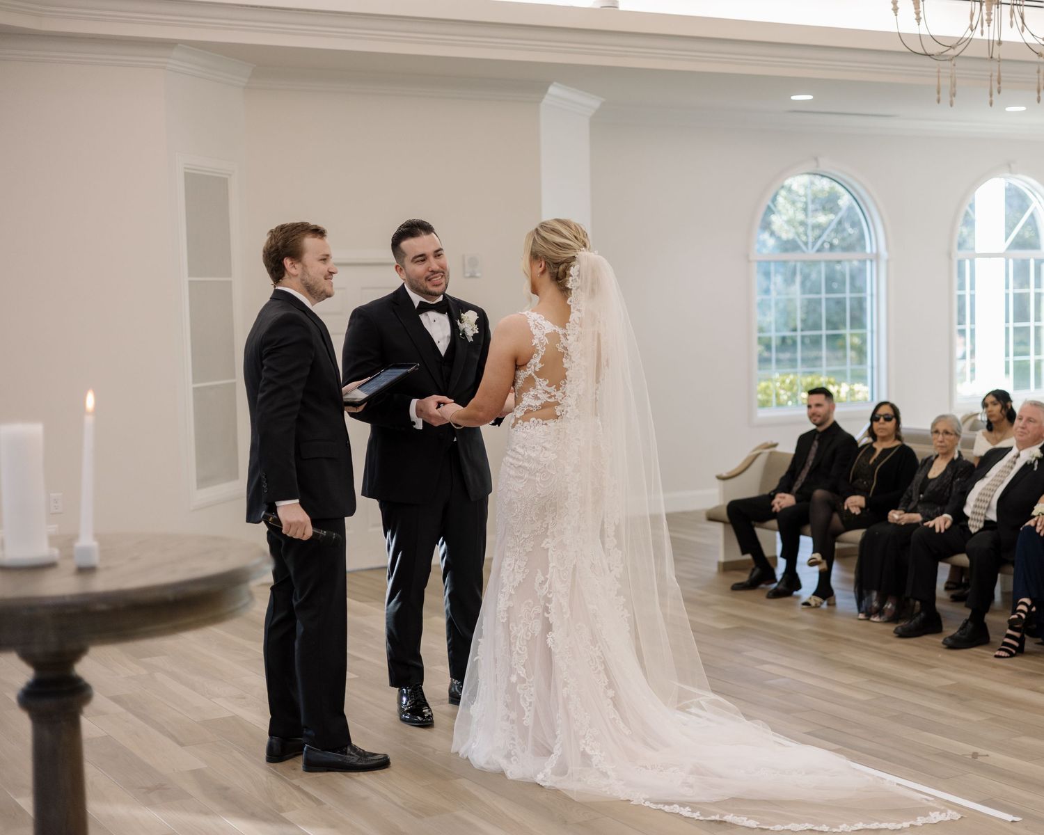 A bride and groom exchange vows at the altar with an officiant in a bright chapel.