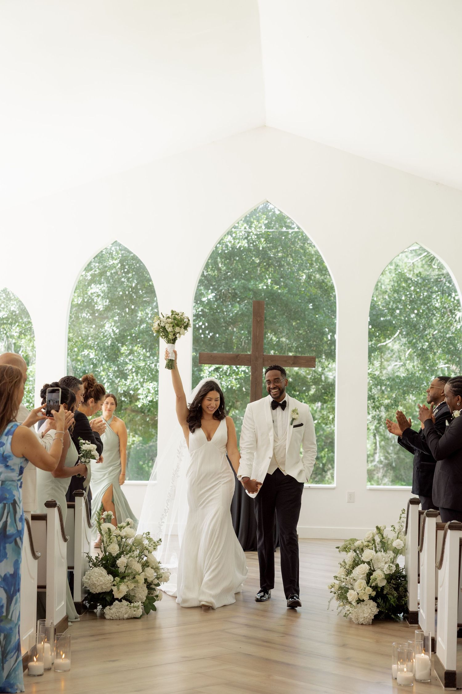 Jubilant bride raises bouquet while walking down aisle with groom after wedding ceremony.
