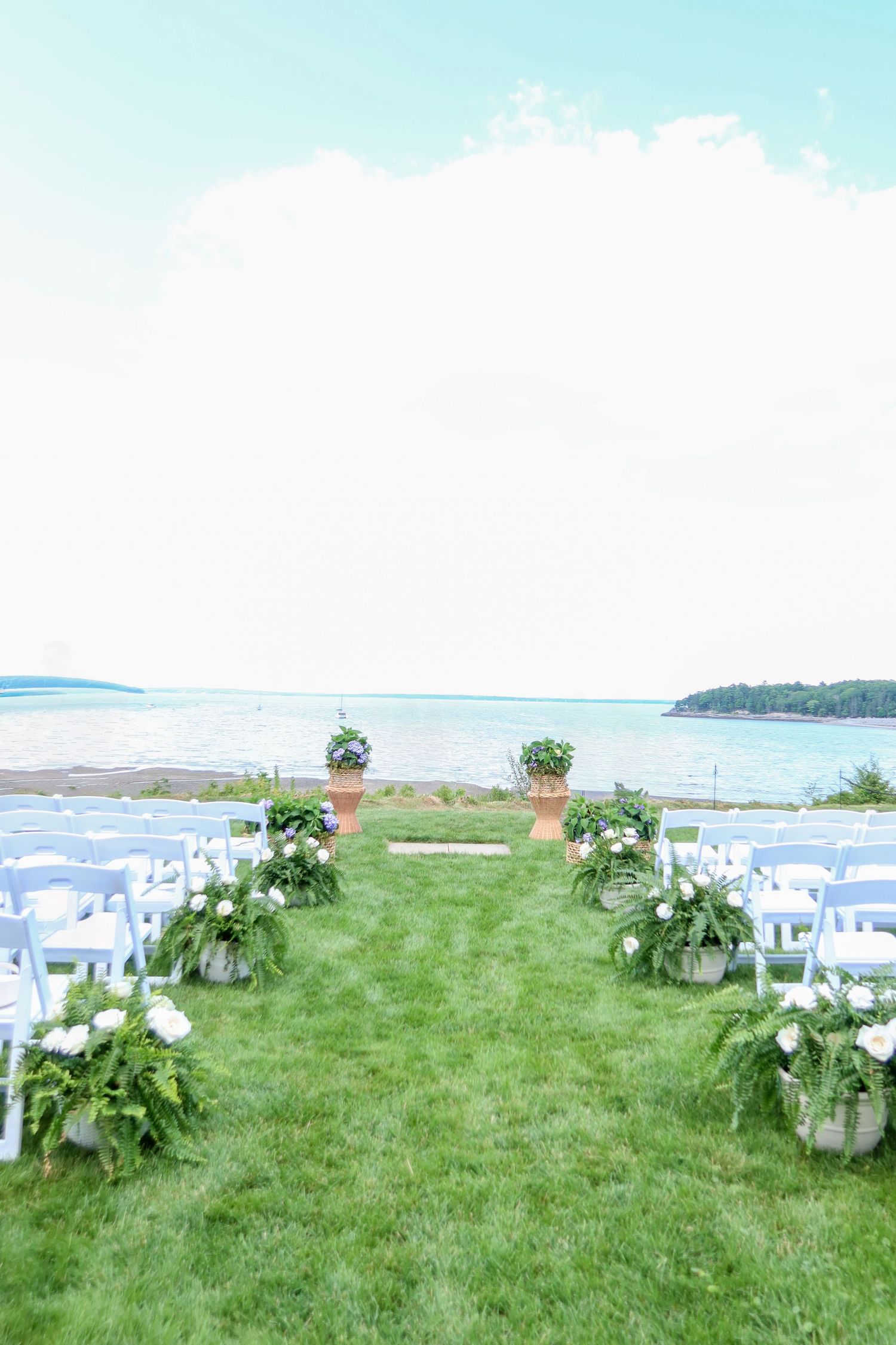 Elegant outdoor waterfront wedding ceremony setup with white chairs and floral aisle decor.