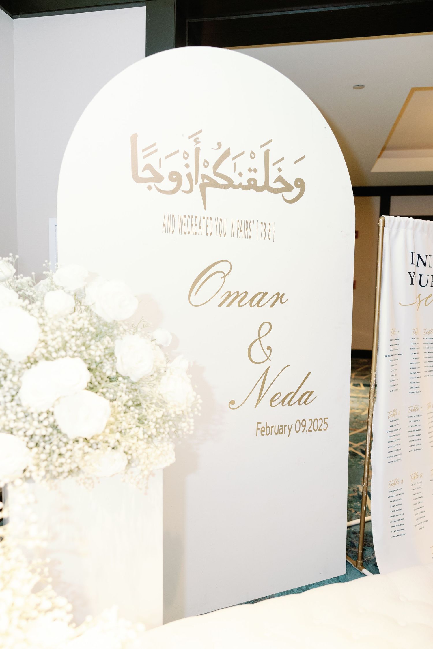 White arched wedding welcome sign reading Omar and Neda February 09 2025 with Arabic script and floral decor.