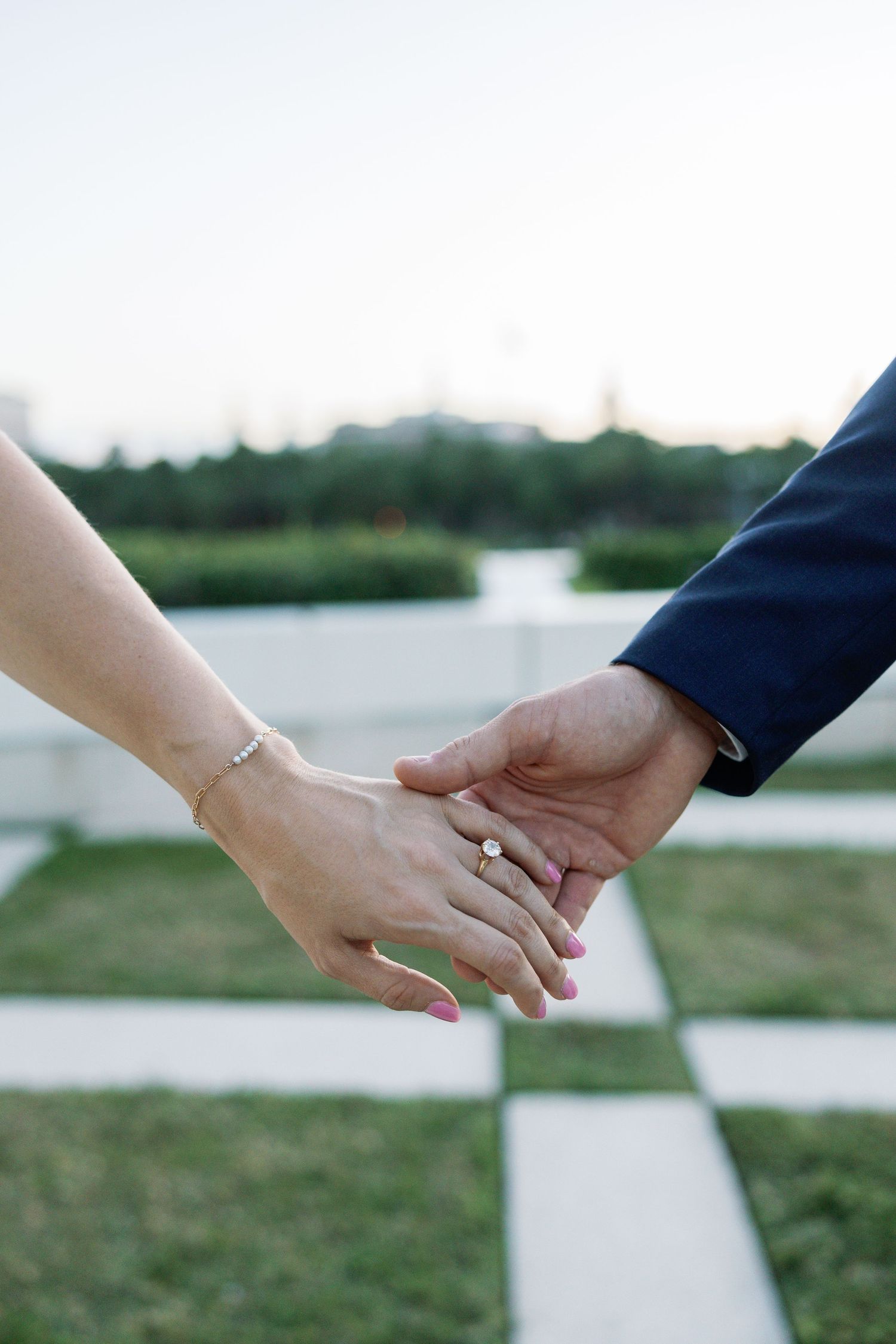 Close-up of couple holding hands showing engagement ring and bracelet outdoors on checkered patio.