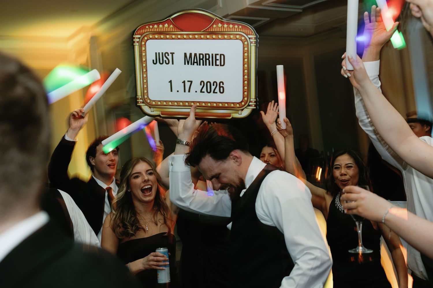 Wedding reception guests celebrating with glow sticks and a Just Married sign dated 1.17.2026.