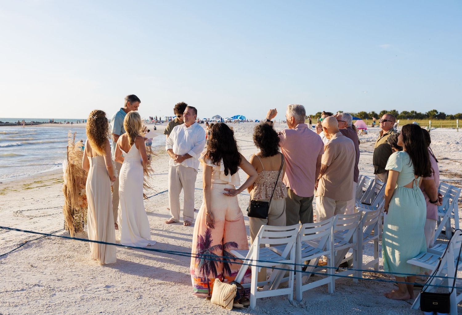 Small intimate beach wedding ceremony with guests gathered on white sand at sunset.