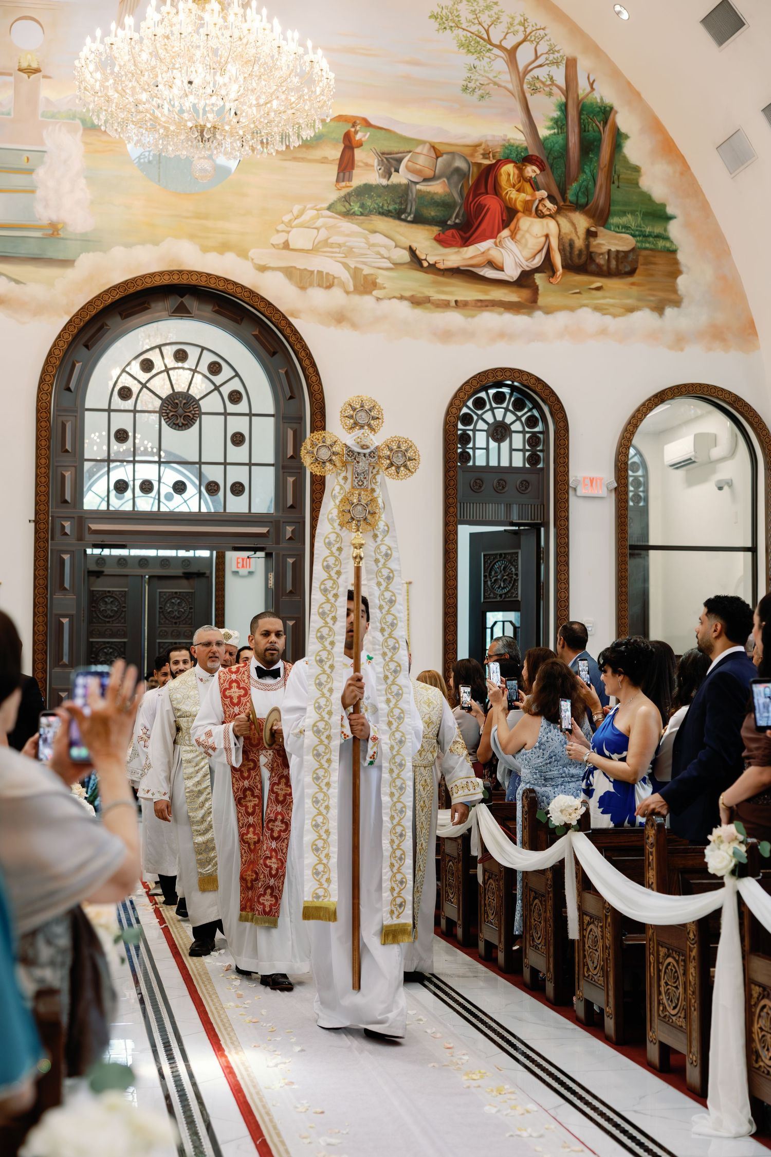 Priests in ornate vestments lead grand wedding processional through beautifully decorated church interior.