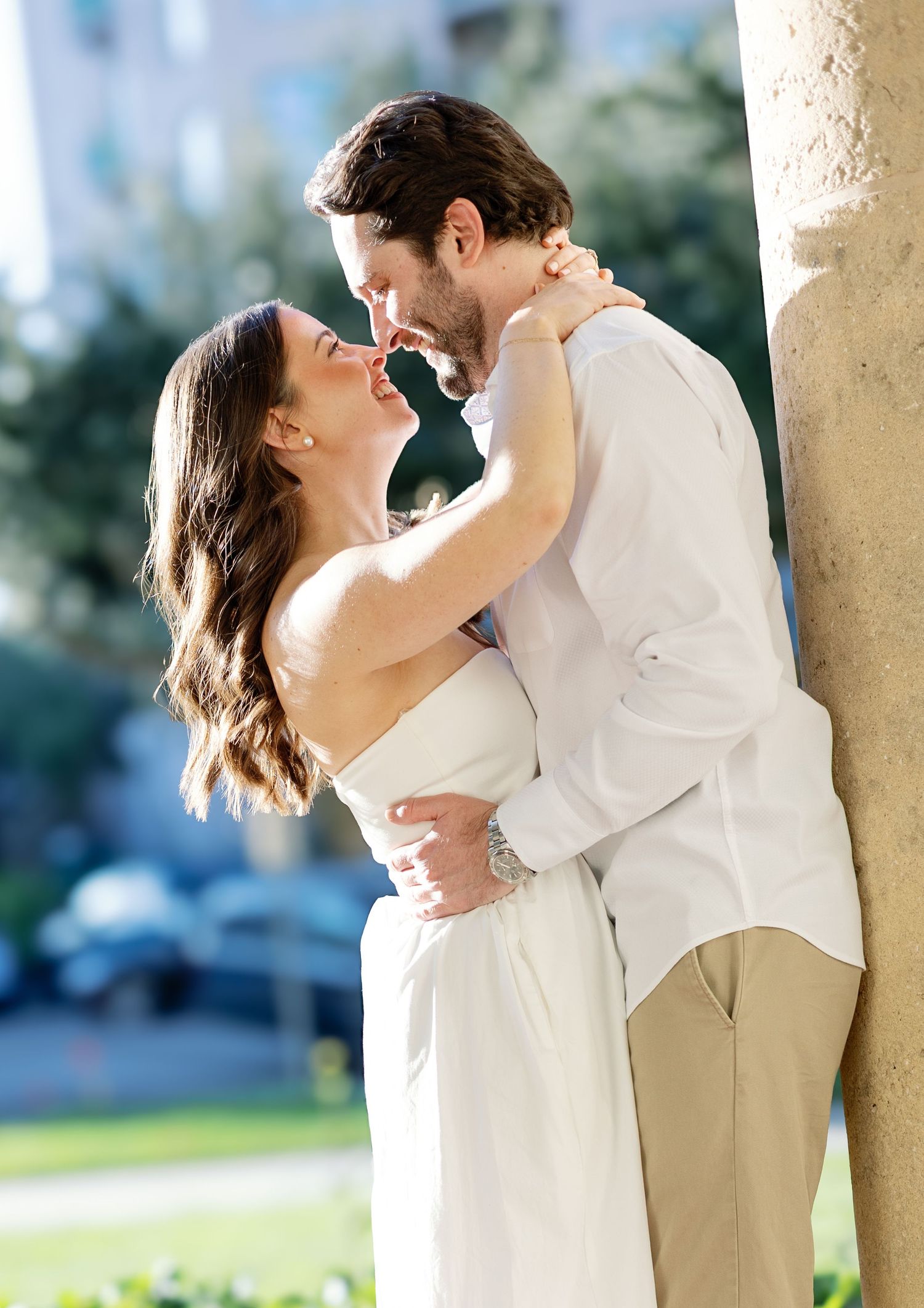 Couple sharing a romantic kiss while leaning against a stone column outdoors.