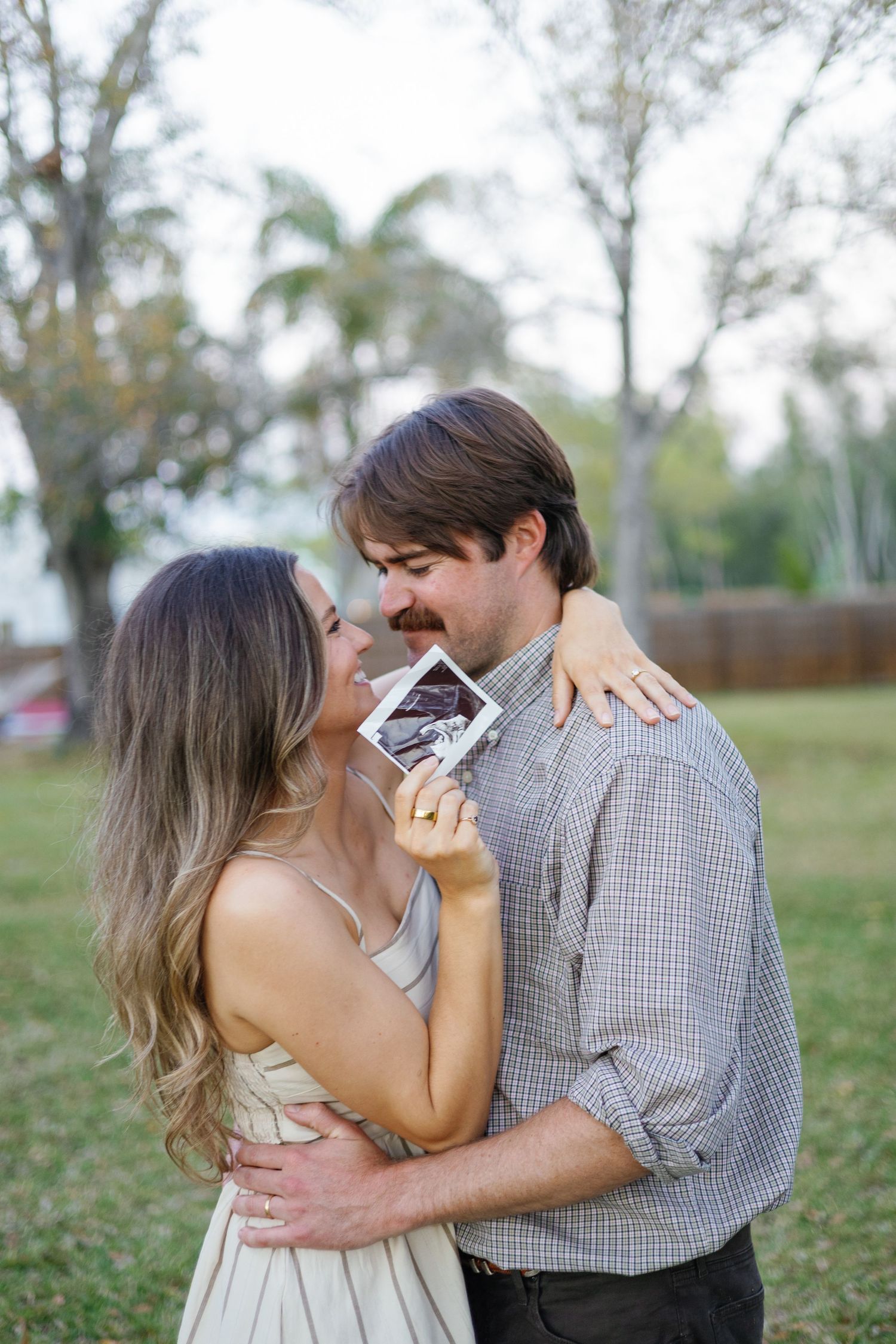 Joyful couple embracing outdoors while holding a pregnancy ultrasound photo.