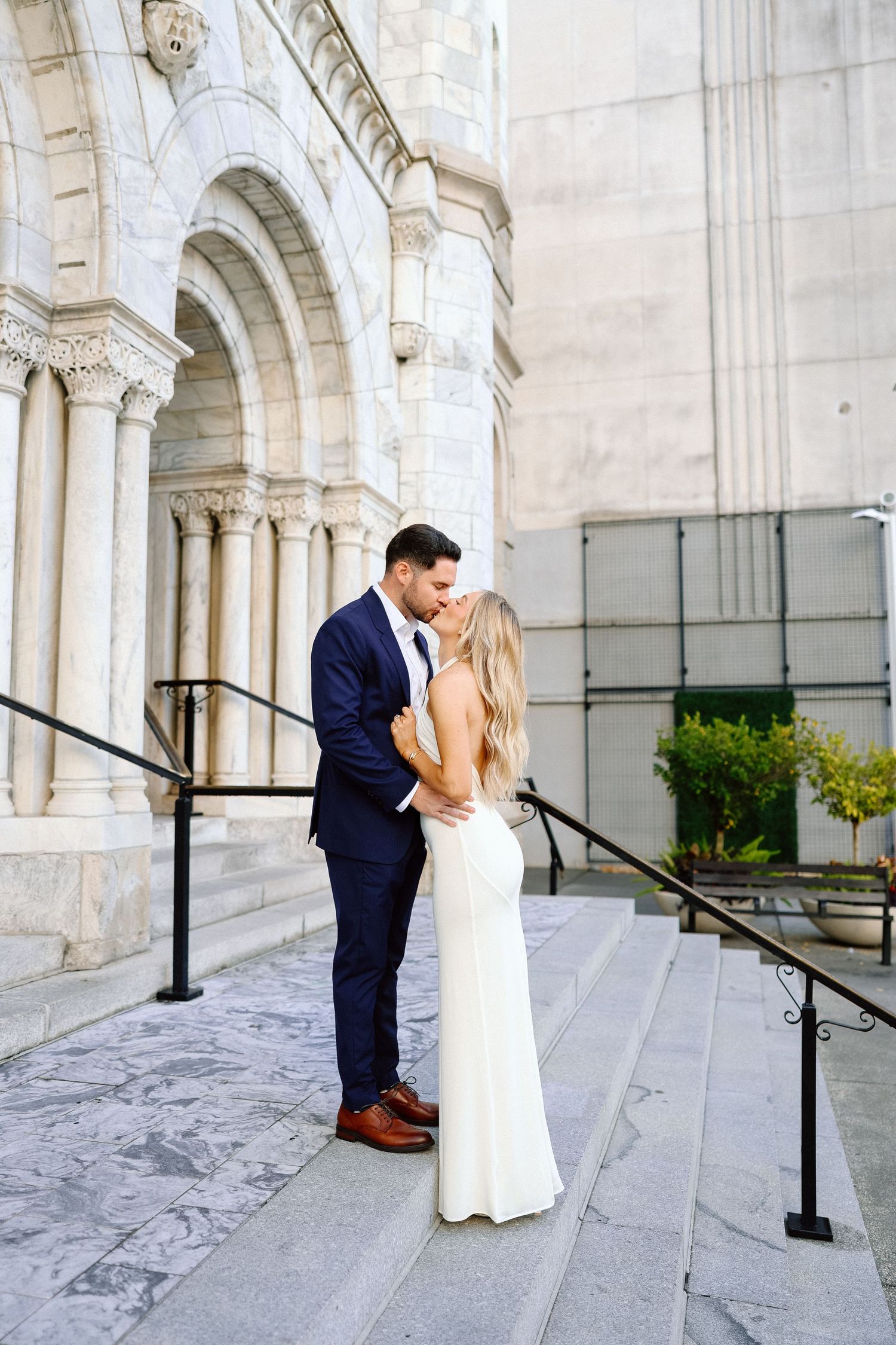 Bride and groom sharing a romantic kiss on marble steps outside an elegant historic building.