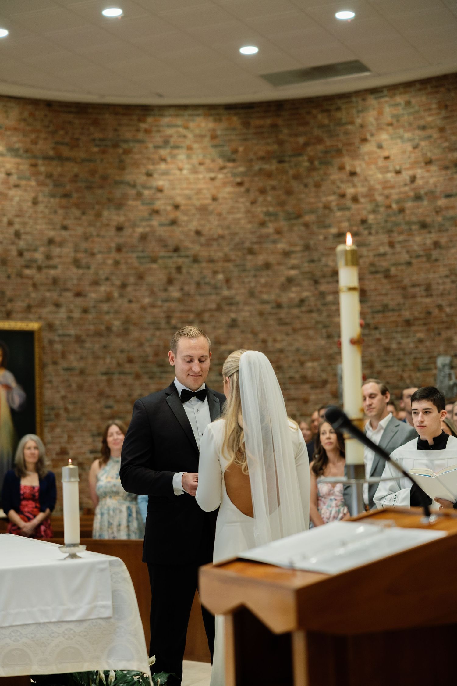 Groom reading wedding vows to bride at altar in brick Catholic church ceremony.