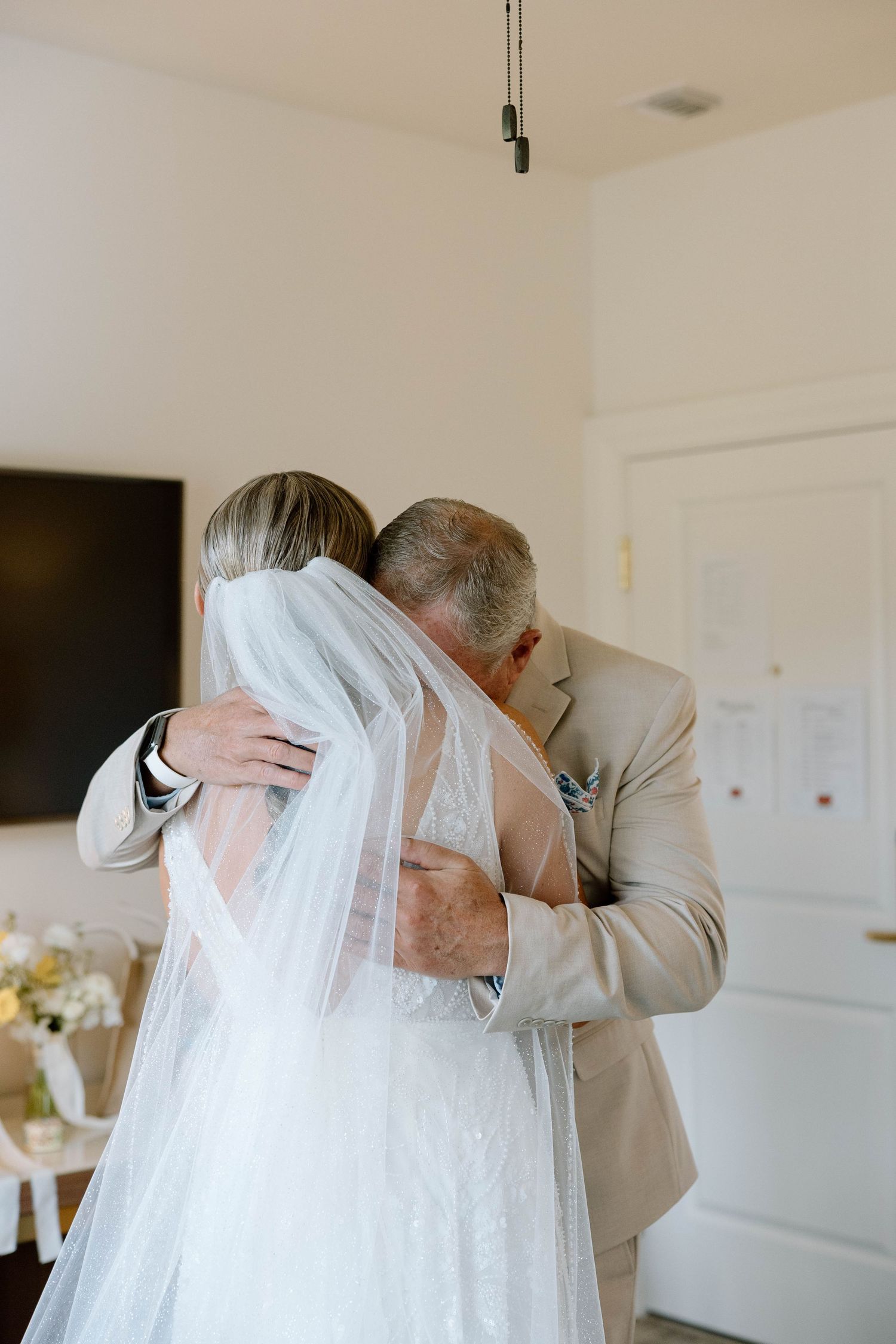 Emotional father of the bride sharing a tender hug with his daughter in her wedding gown and veil.