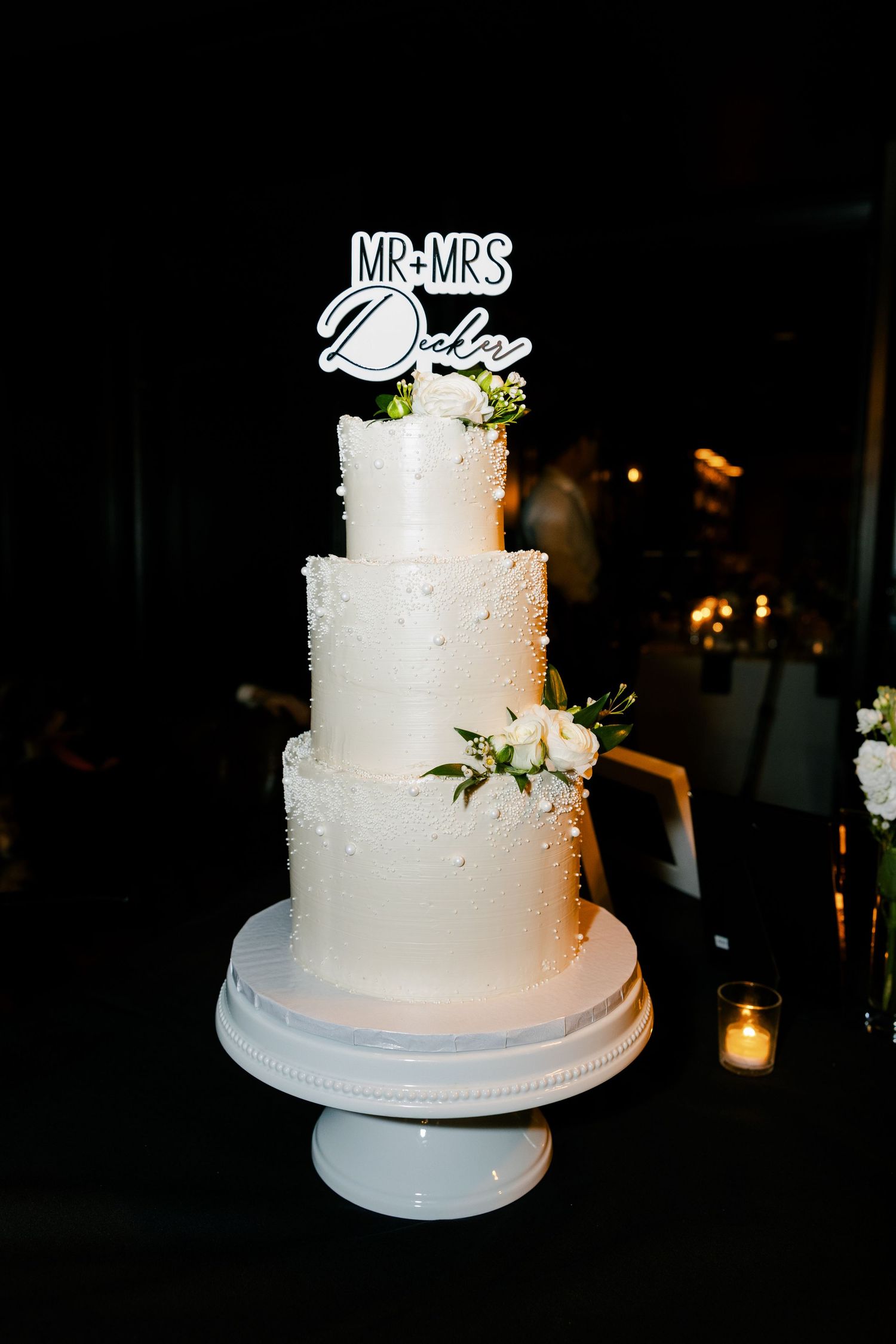 Elegant four-tier white wedding cake with pearl details and floral accents topped with Mr. and Mrs. topper.