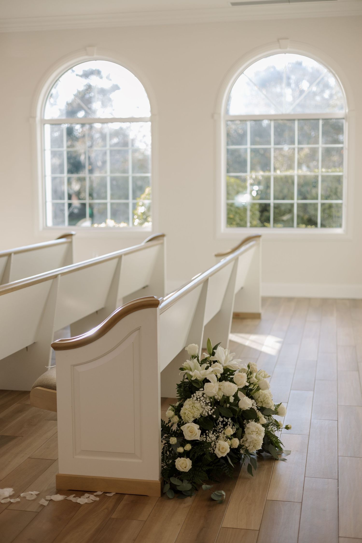 White floral arrangement adorns the end of a wooden church pew in a bright chapel.