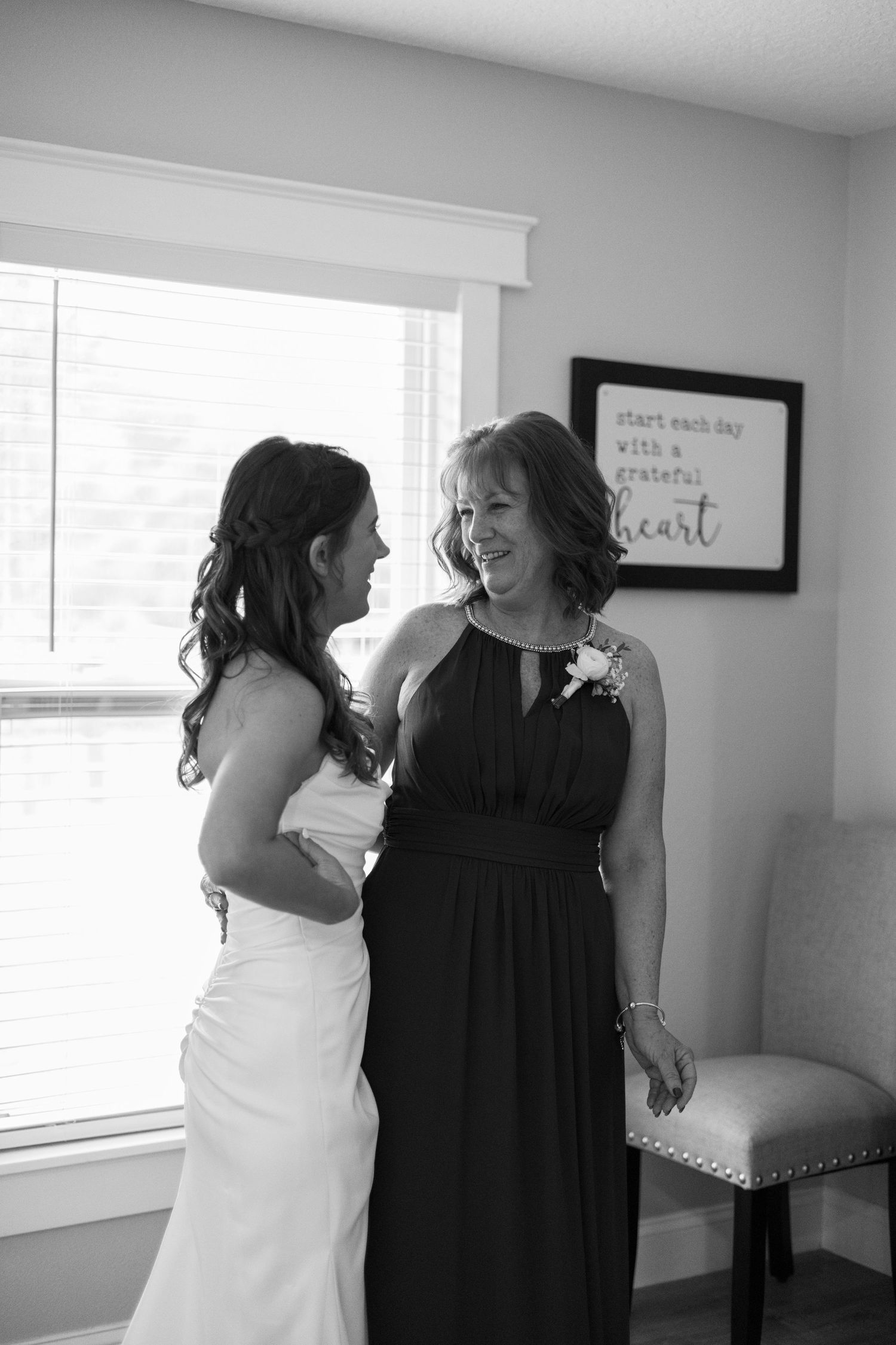 Black and white photo of a bride in white gown sharing a joyful moment with her mother indoors.
