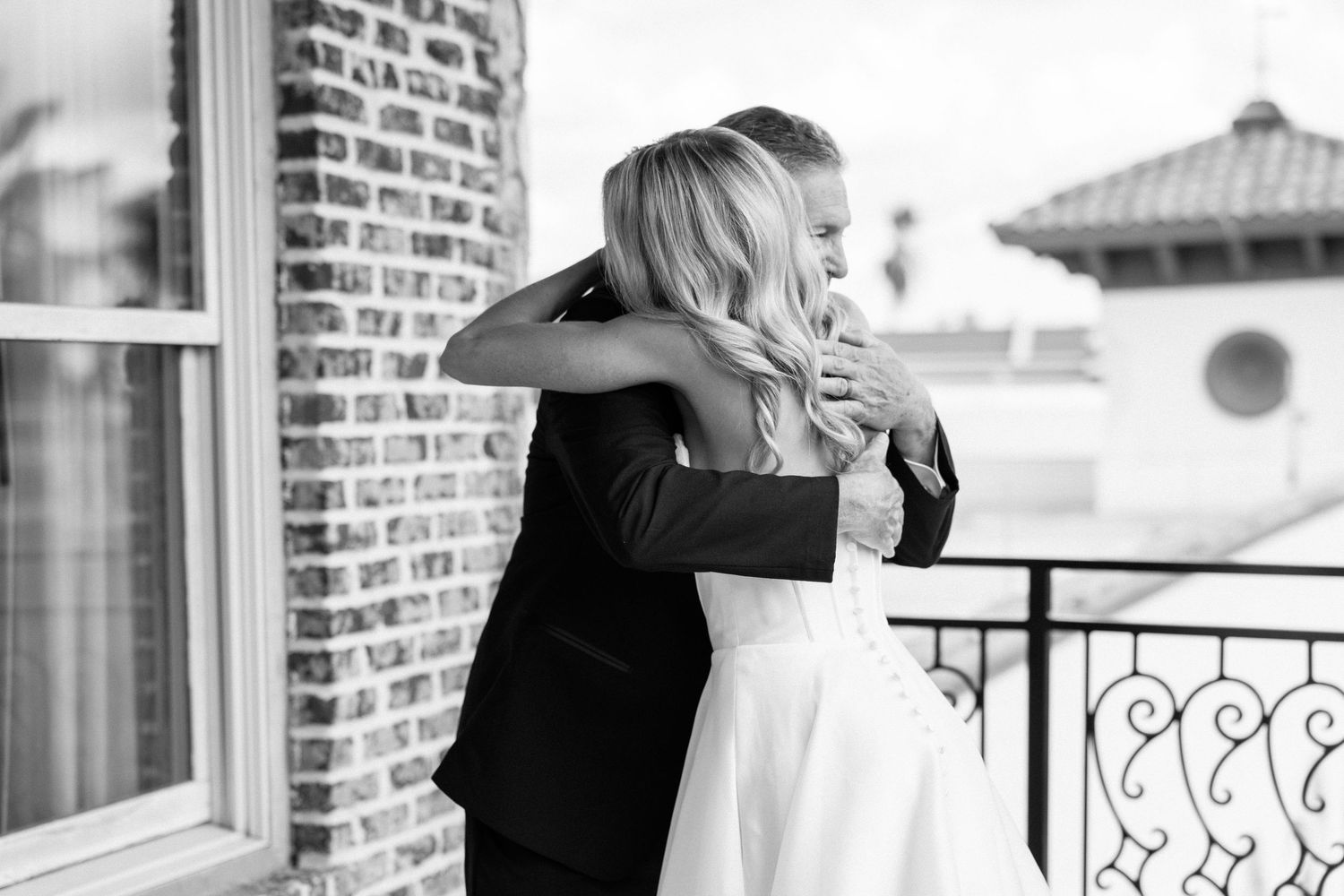 Black and white photo of bride and groom sharing tender first look embrace on outdoor brick balcony.