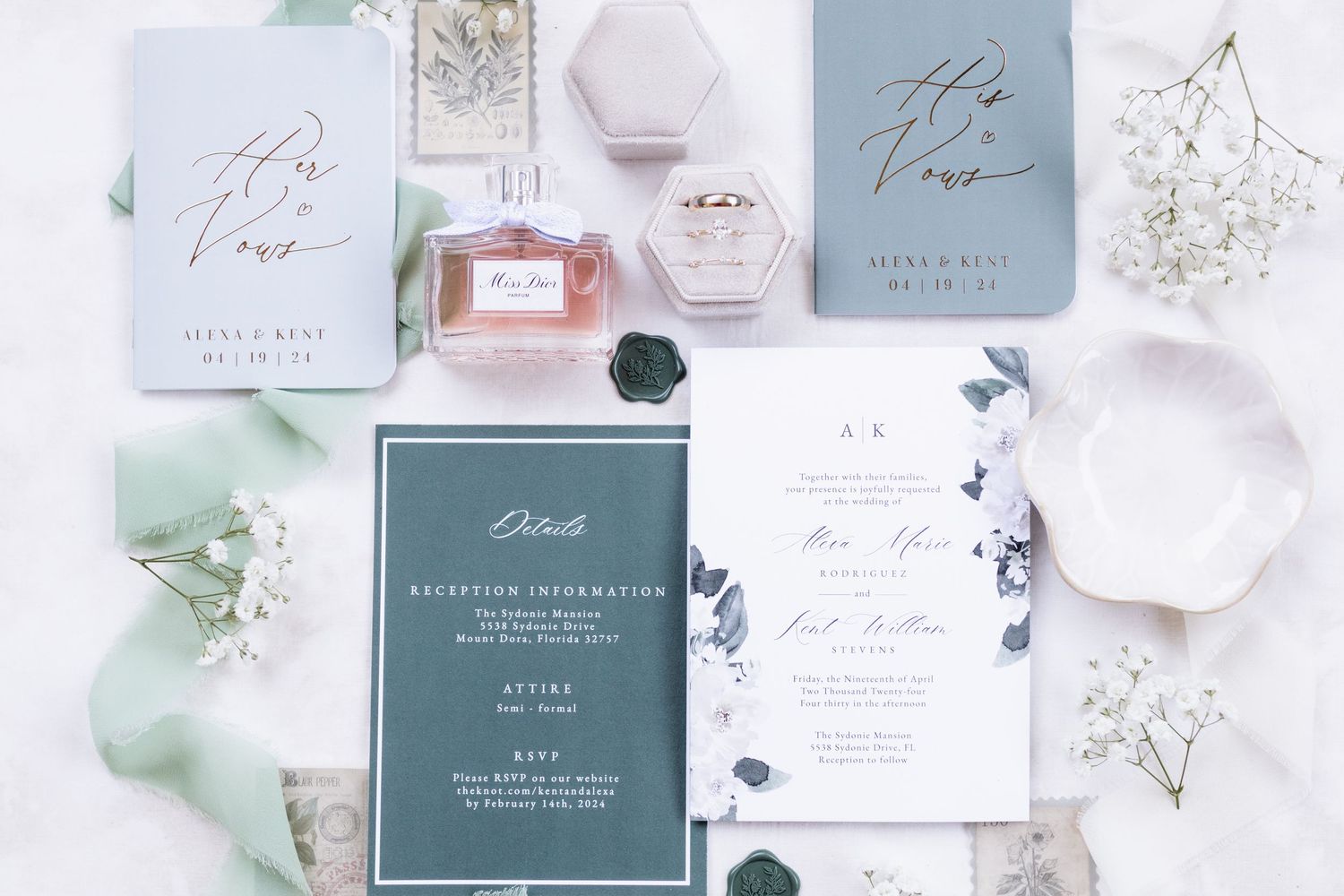 Elegant wedding stationery flatlay with dusty blue invitations, perfume bottle, and baby's breath.